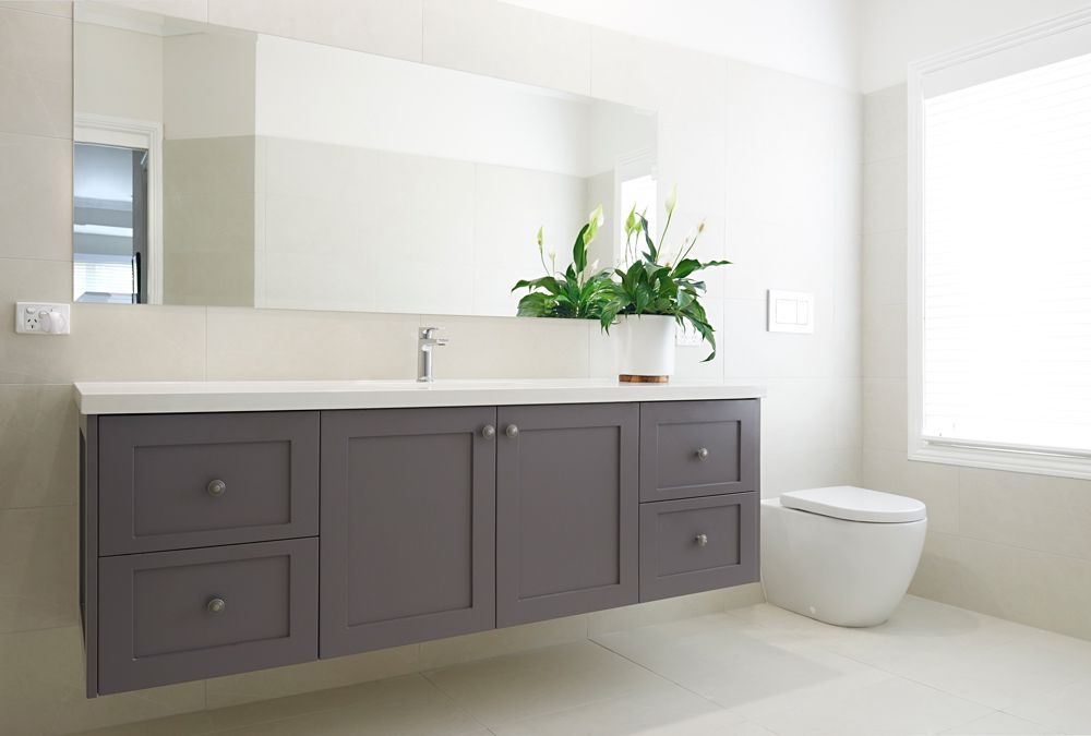 Modern bathroom with gray vanity, large mirror, white toilet, and white flowers on the counter