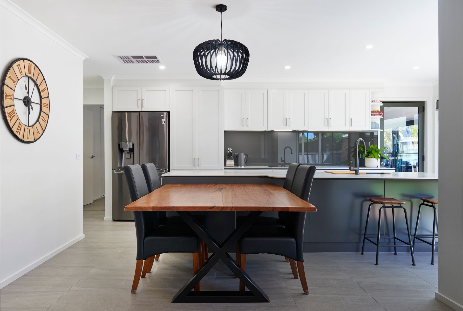Modern kitchen and dining area with white cabinets, stainless fridge, wooden table, and black chairs