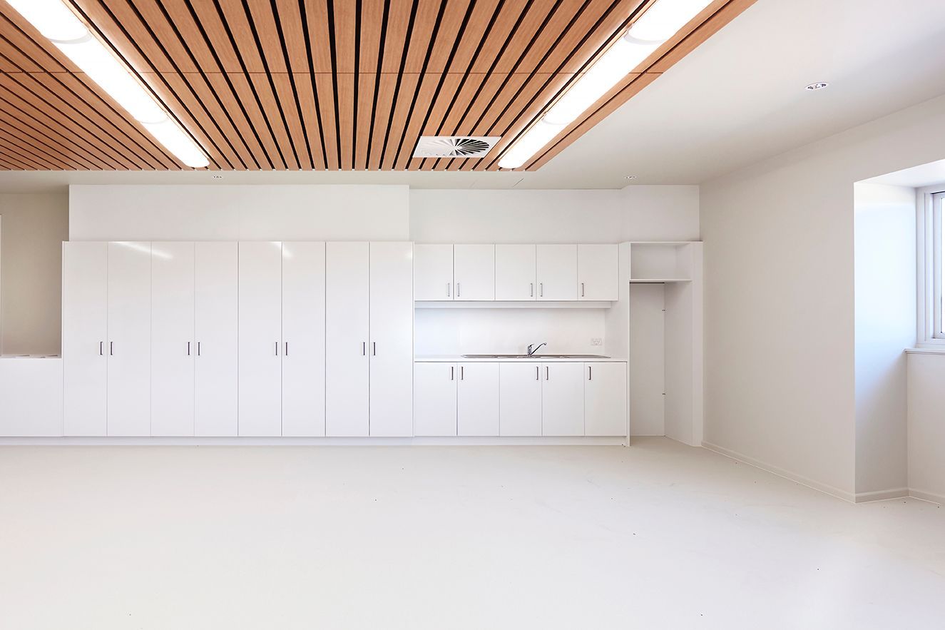 Bright empty modern kitchen with white cabinets, wood-slat ceiling, and large window