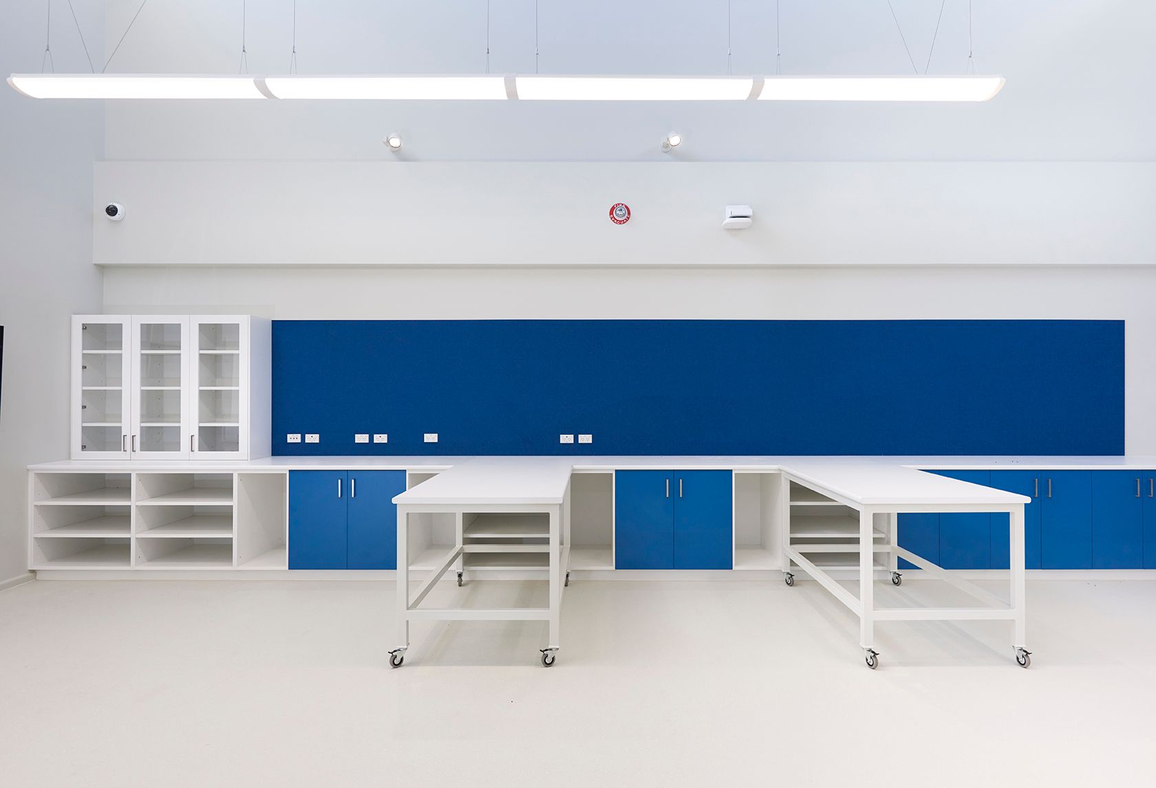 Bright white classroom with blue cabinets, storage shelves, and work tables along the wall