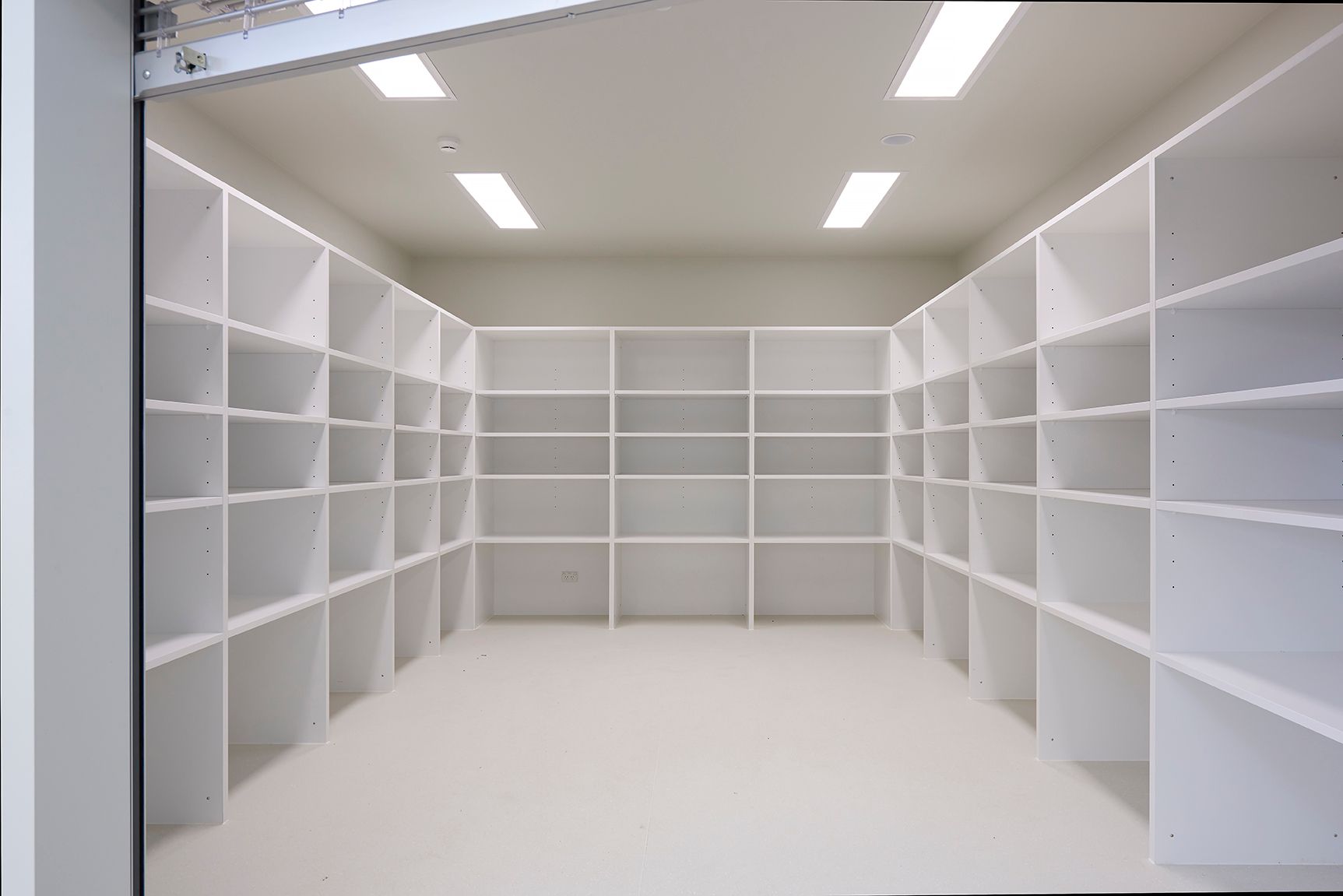 Empty white storage room with built-in shelves and overhead lights