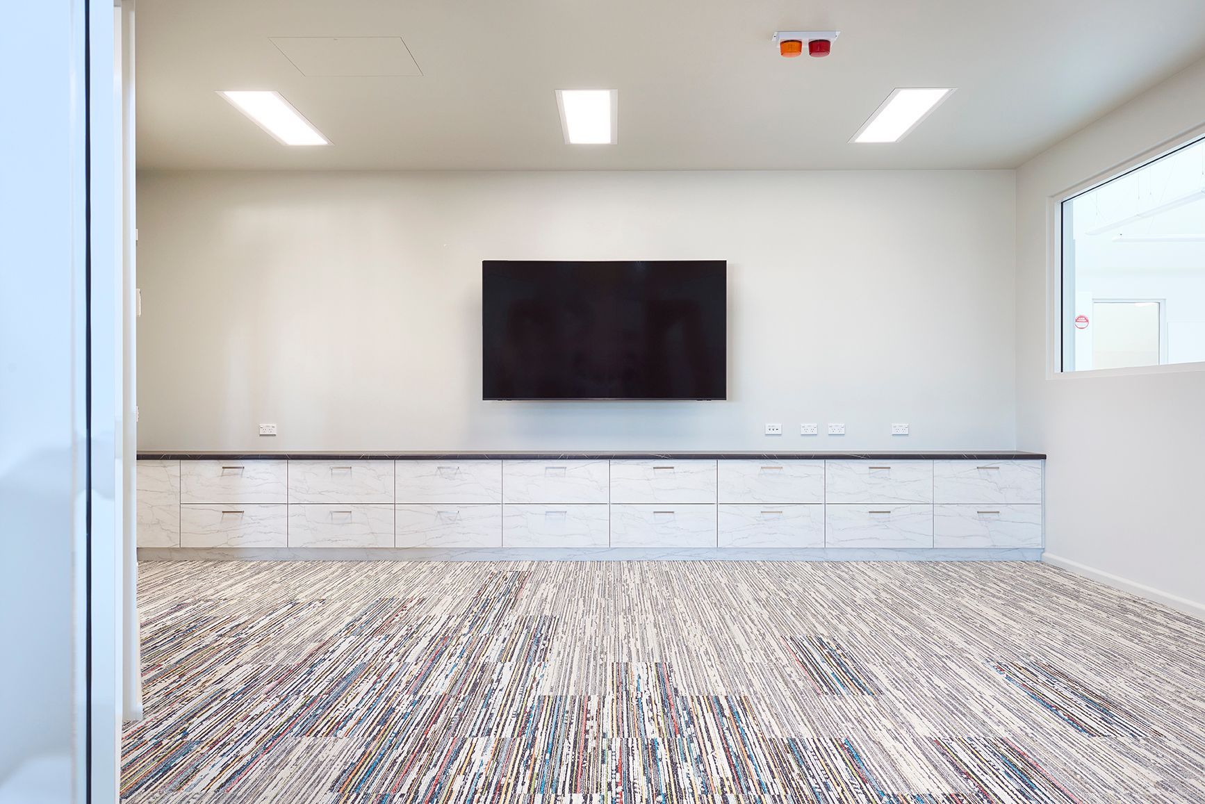 Bright empty conference room with wall-mounted TV, white cabinets, and patterned carpet