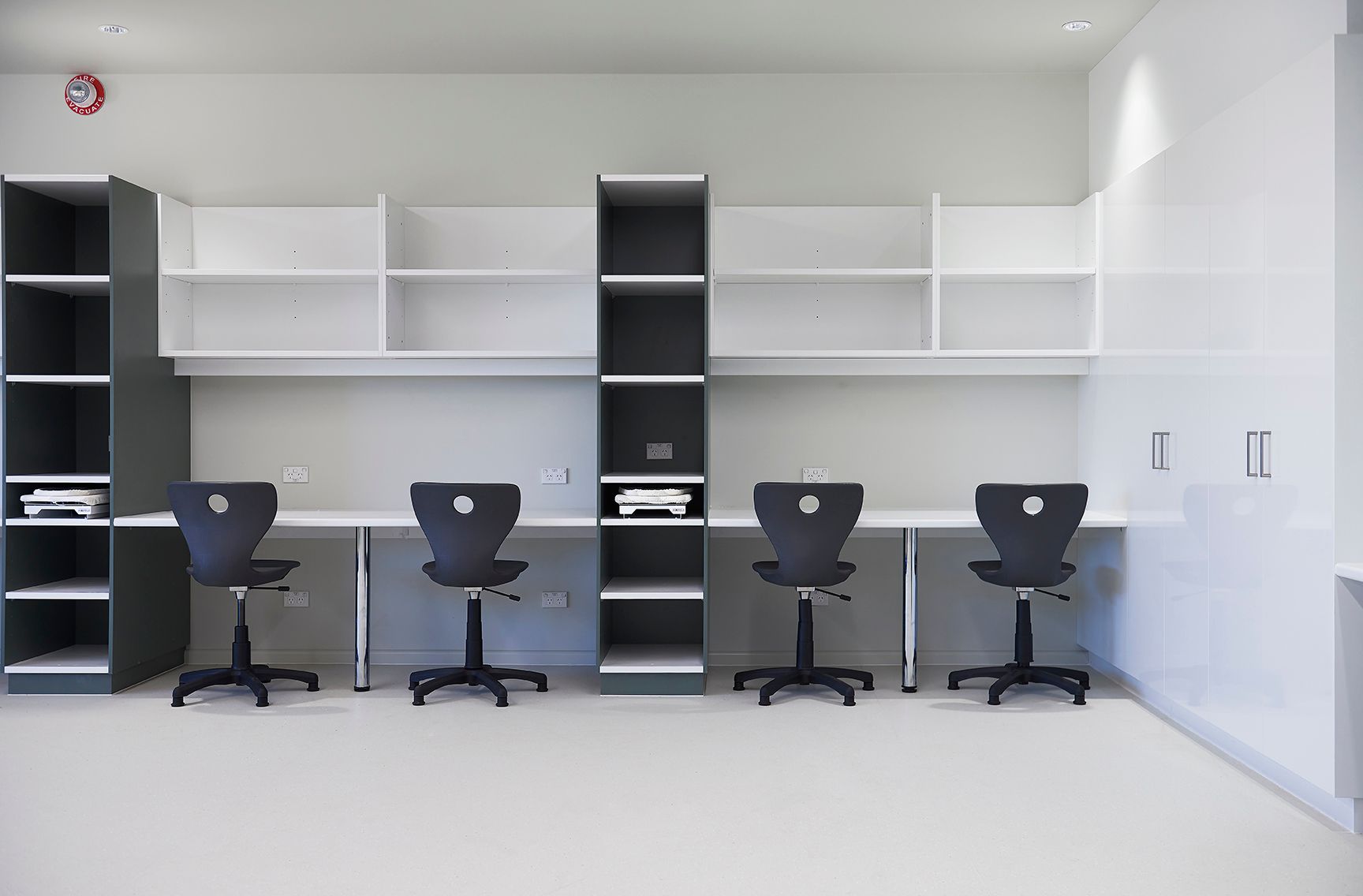 Minimal white office with four black swivel chairs at built-in desks and shelving.