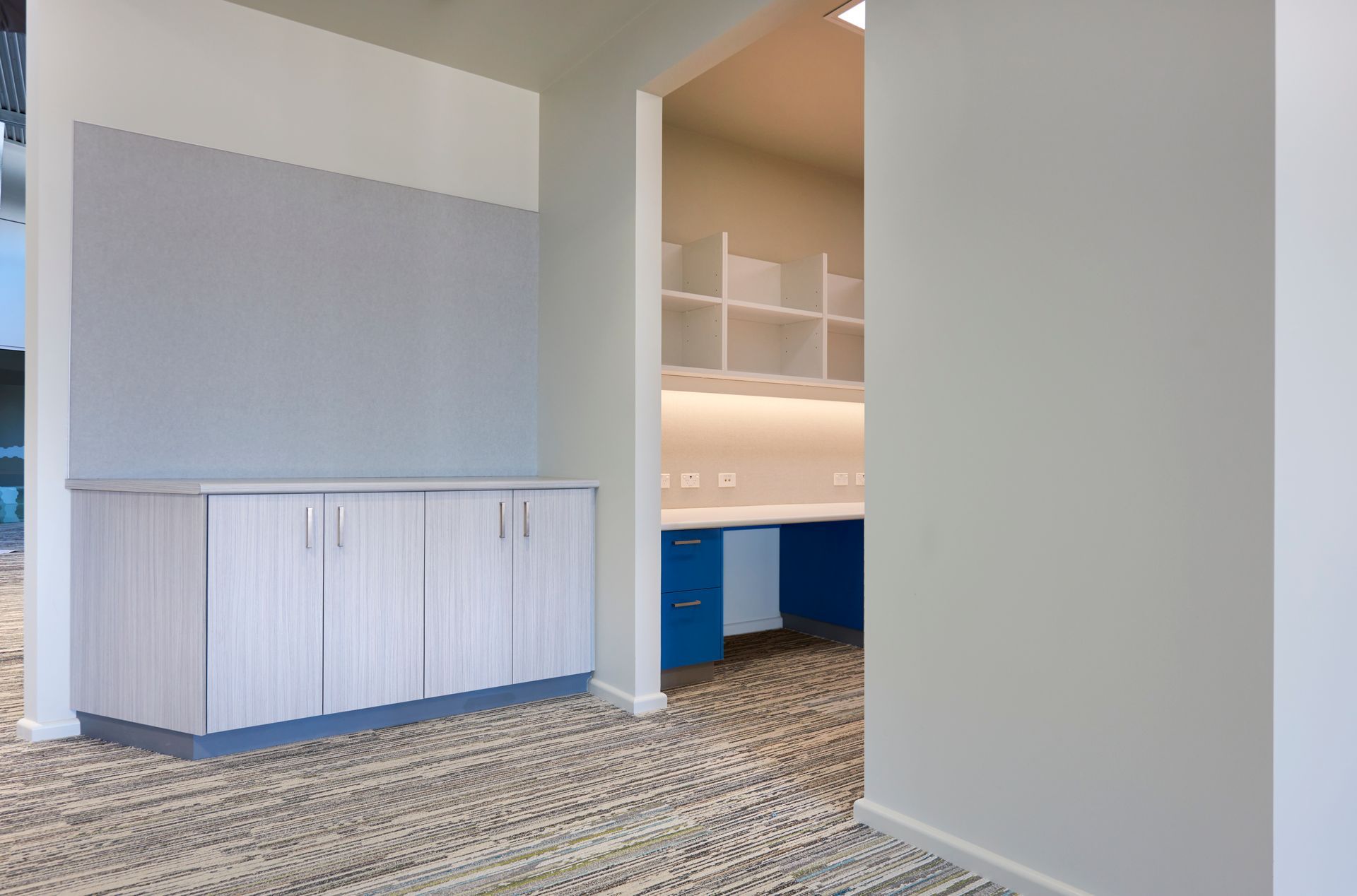 Modern office reception area with built-in cabinets, blue desk, and carpeted floor