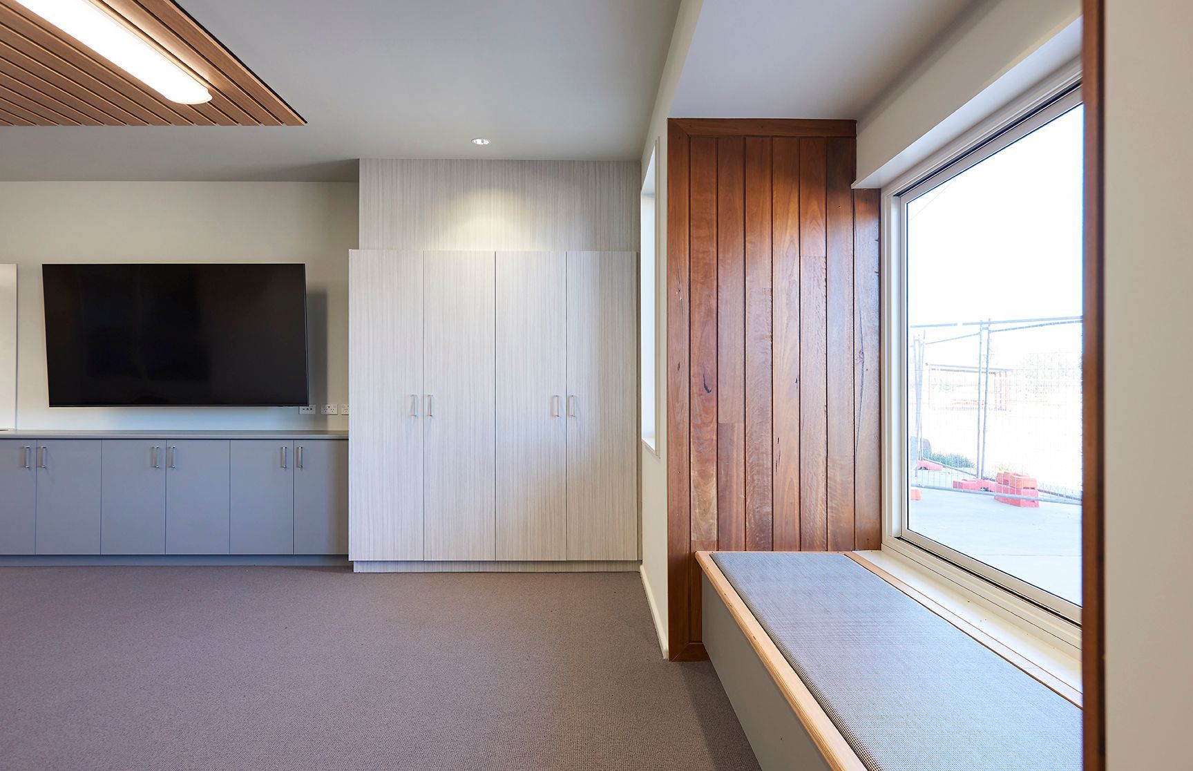 Modern room with TV cabinet, white closet, and a large window seat by wooden paneling