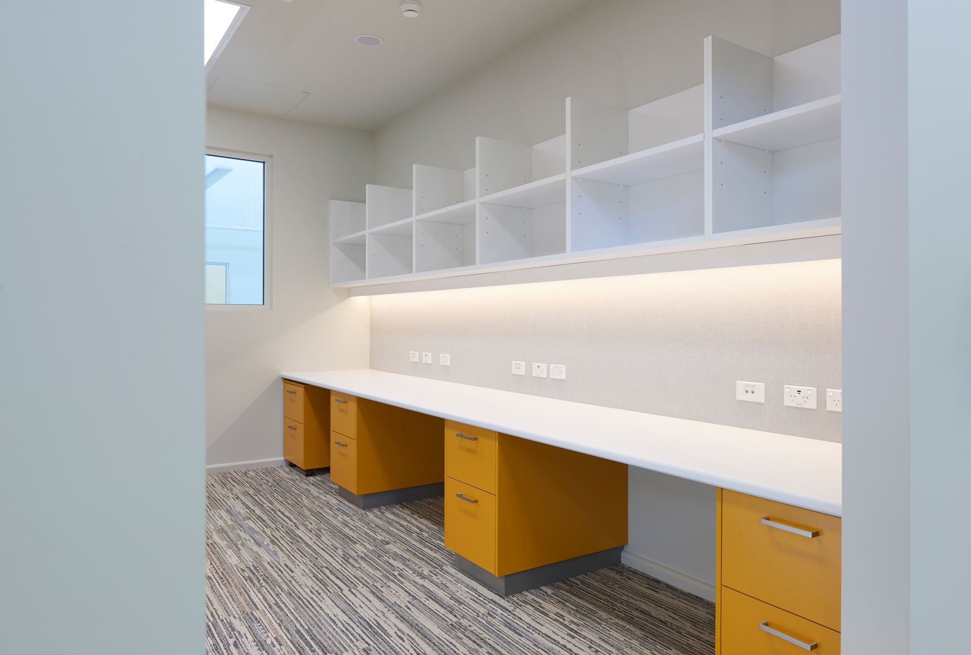 Modern study room with white built-in desks, yellow drawers, and open shelving