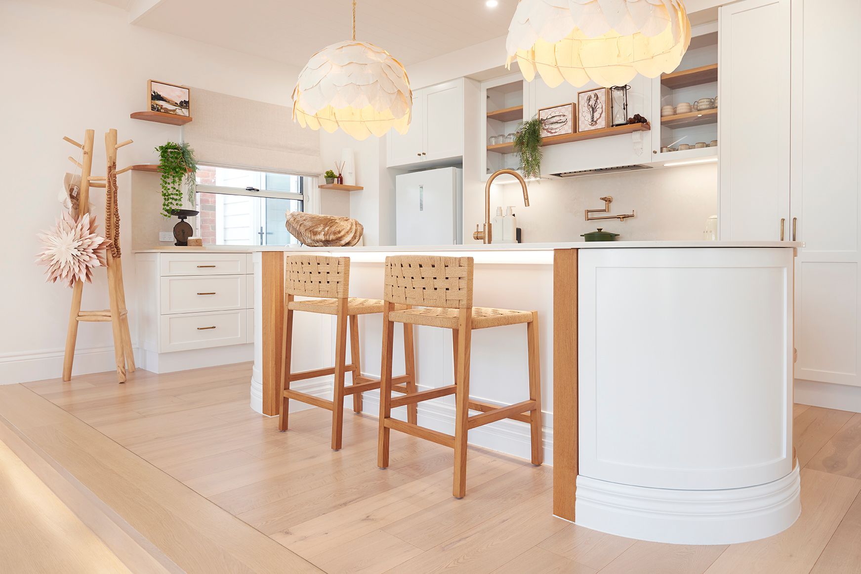 Bright, white kitchen with island, two woven bar stools, and two pendant lights.