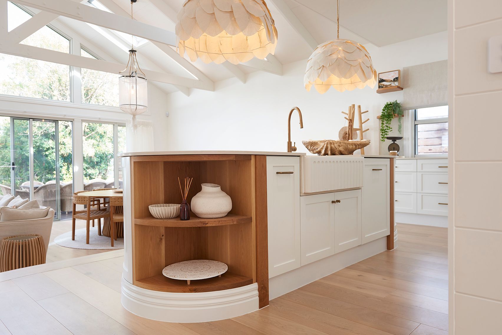 Bright white kitchen island with wooden shelves and hanging pendant lights in a sunlit modern interior