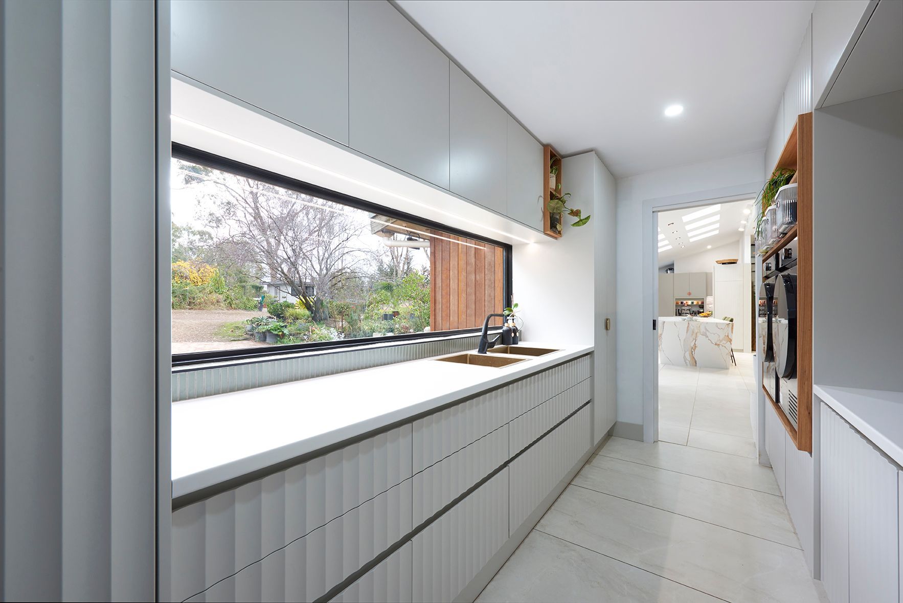 Bright modern kitchen hallway with white counters, skylight, and window view of trees