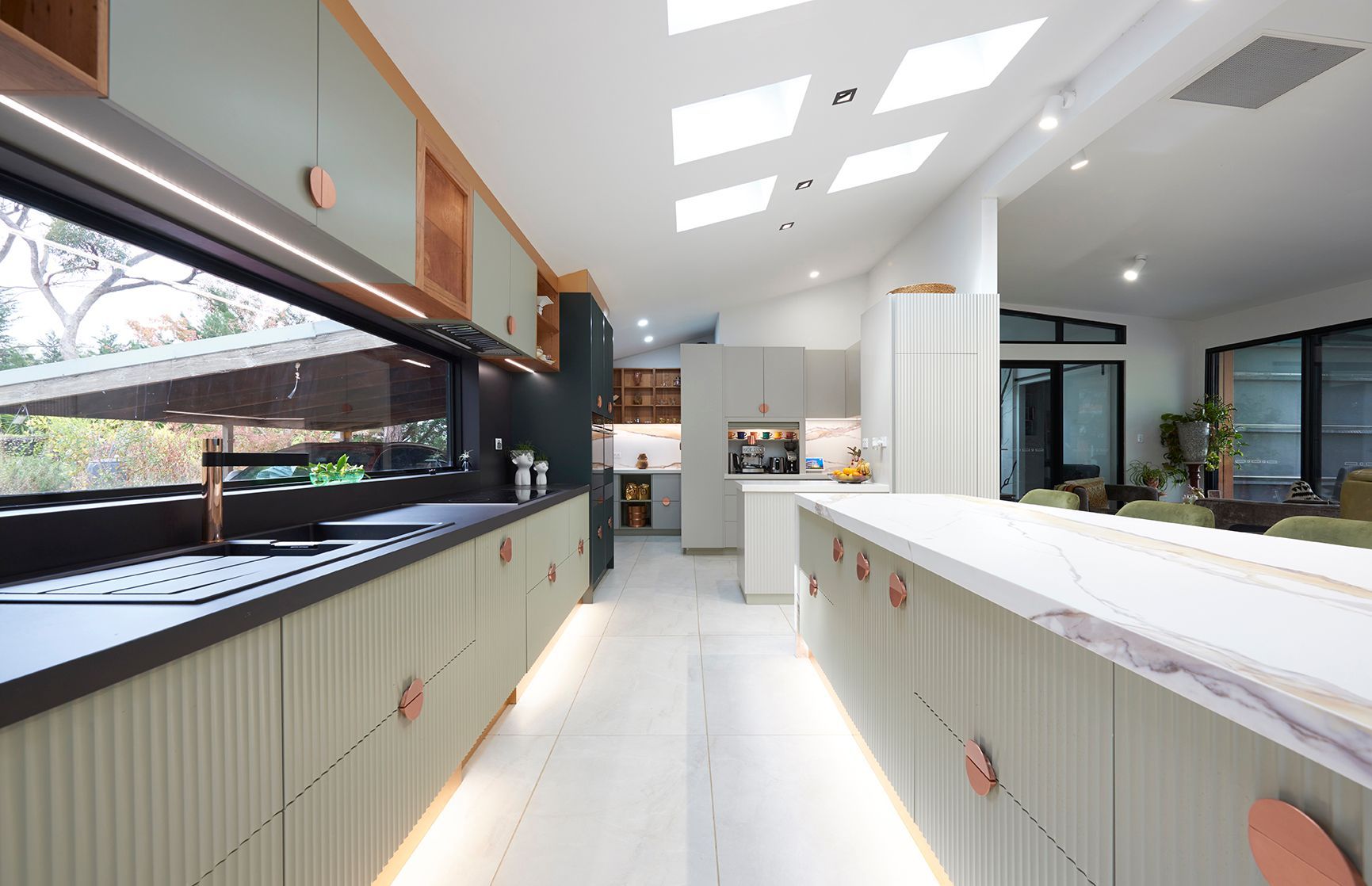 Bright modern kitchen with white counters, skylights, and large glass-front display cases