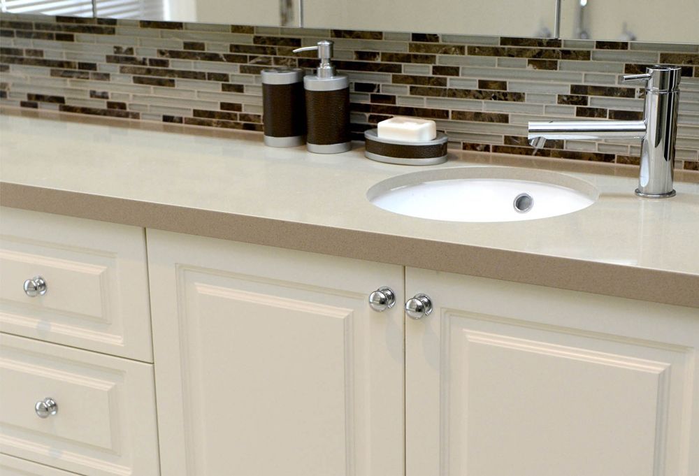 Cream bathroom vanity with white sink, chrome faucet, and brown-and-beige tile backsplash.