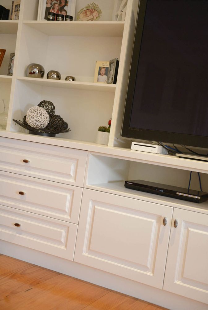 White built-in shelving and cabinets with a large TV, decor items, and a wooden floor.
