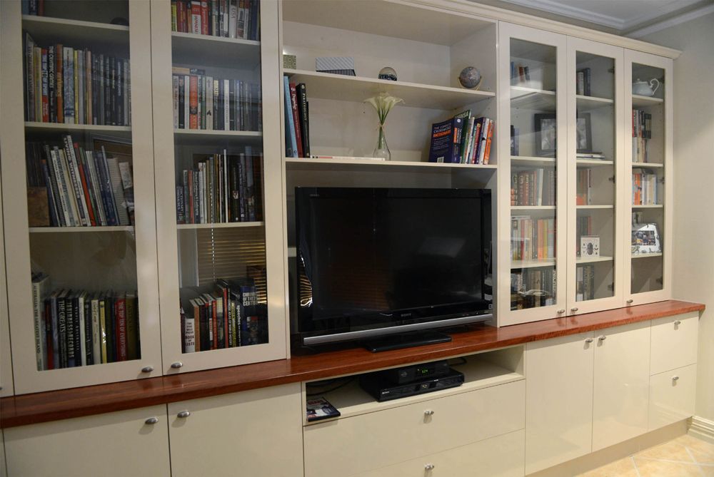 Built-in white bookcases with books, glass cabinets, and a flat-screen TV above cabinets.