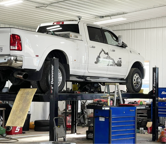 White pickup truck raised on a lift in a garage workshop with tools and equipment nearby | Elite Automotive & Diesel Repair