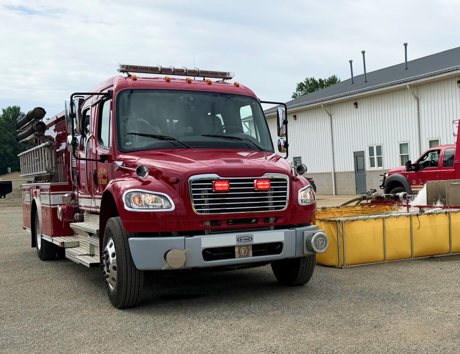 Red emergency utility truck parked beside a building and yellow barriers on a gravel lot. | Elite Automotive & Diesel Repair
