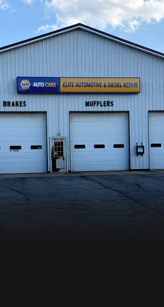 Auto repair shop exterior with blue siding, garage doors, and signs for brakes and mufflers