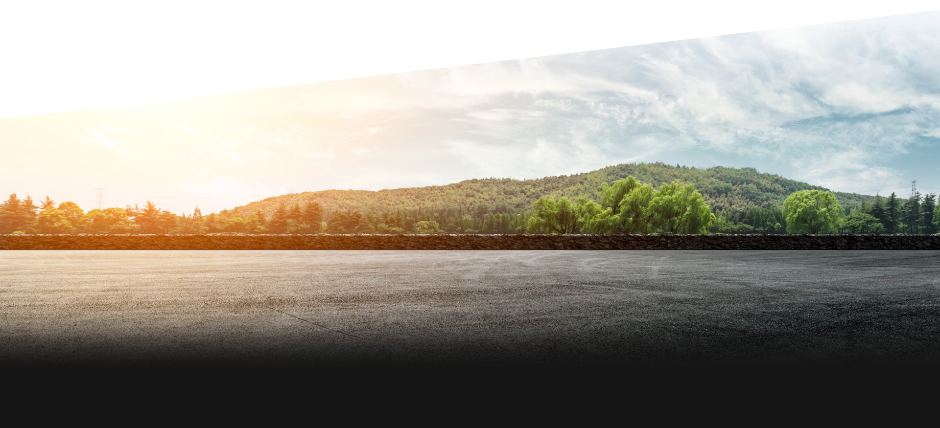 Sunlit forested hill across calm water, with bright sky and dark shoreline foreground | Elite Automotive & Diesel Repair