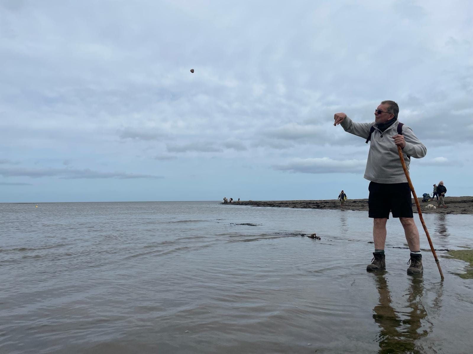 A man is standing in the water on a beach holding a stick.