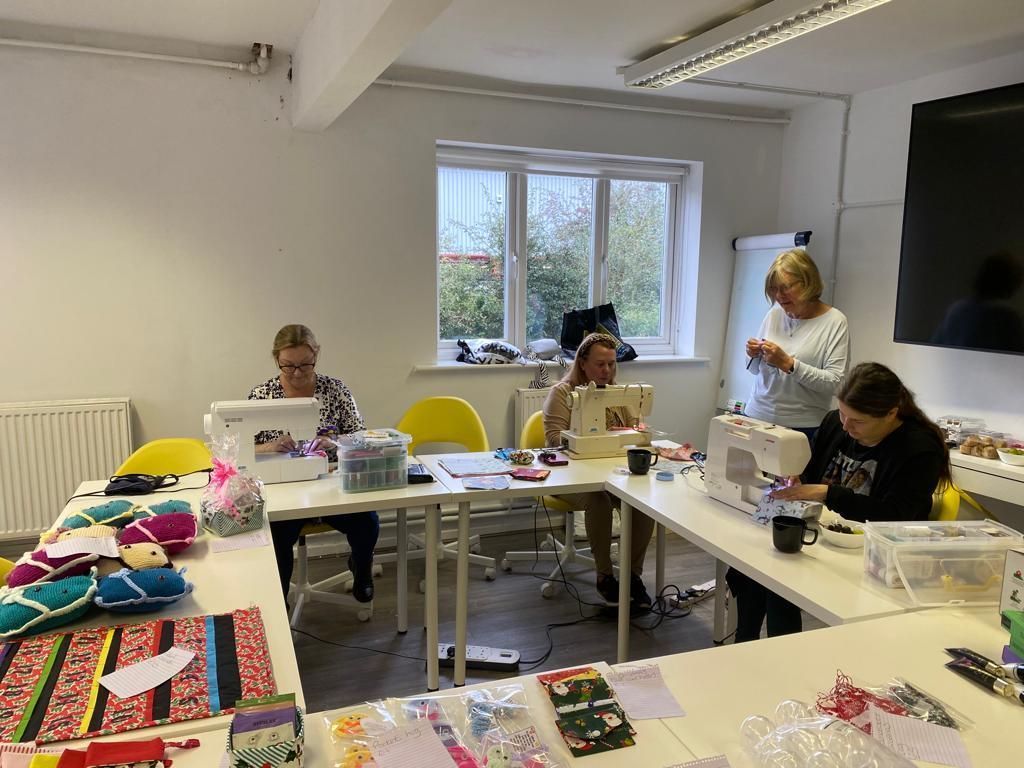 a group of people are sitting at tables in a room using sewing machines .