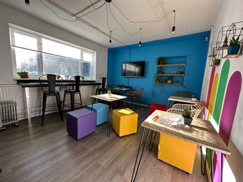 a room with tables , chairs , ottomans and a television on the wall .