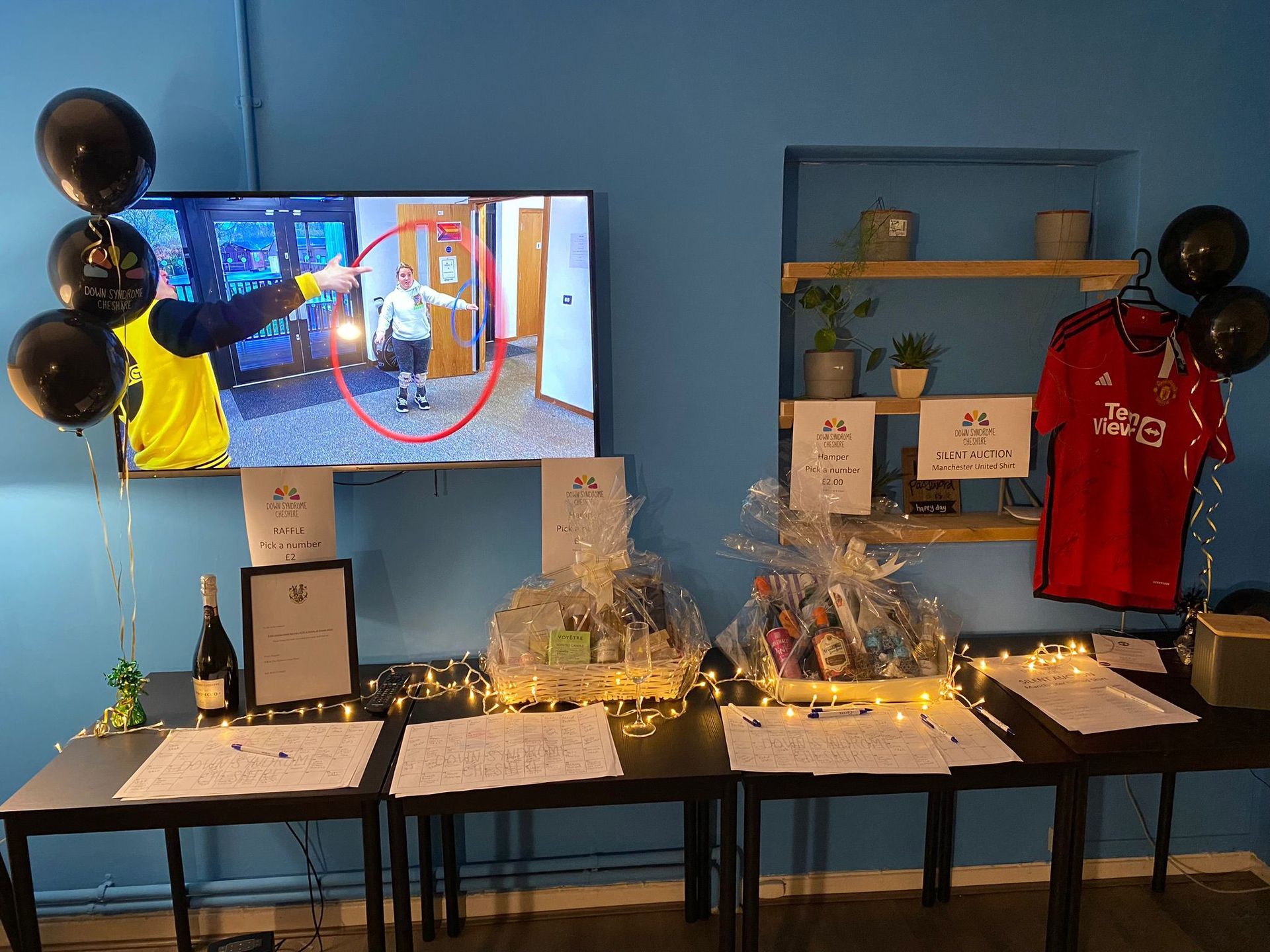 a room with a television , tables , balloons and a red shirt hanging on the wall .