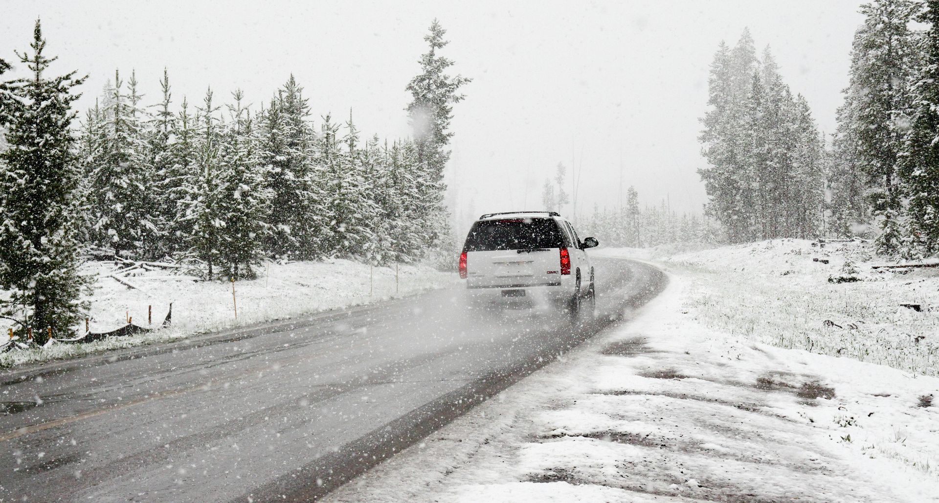 A white suv is driving down a snowy road