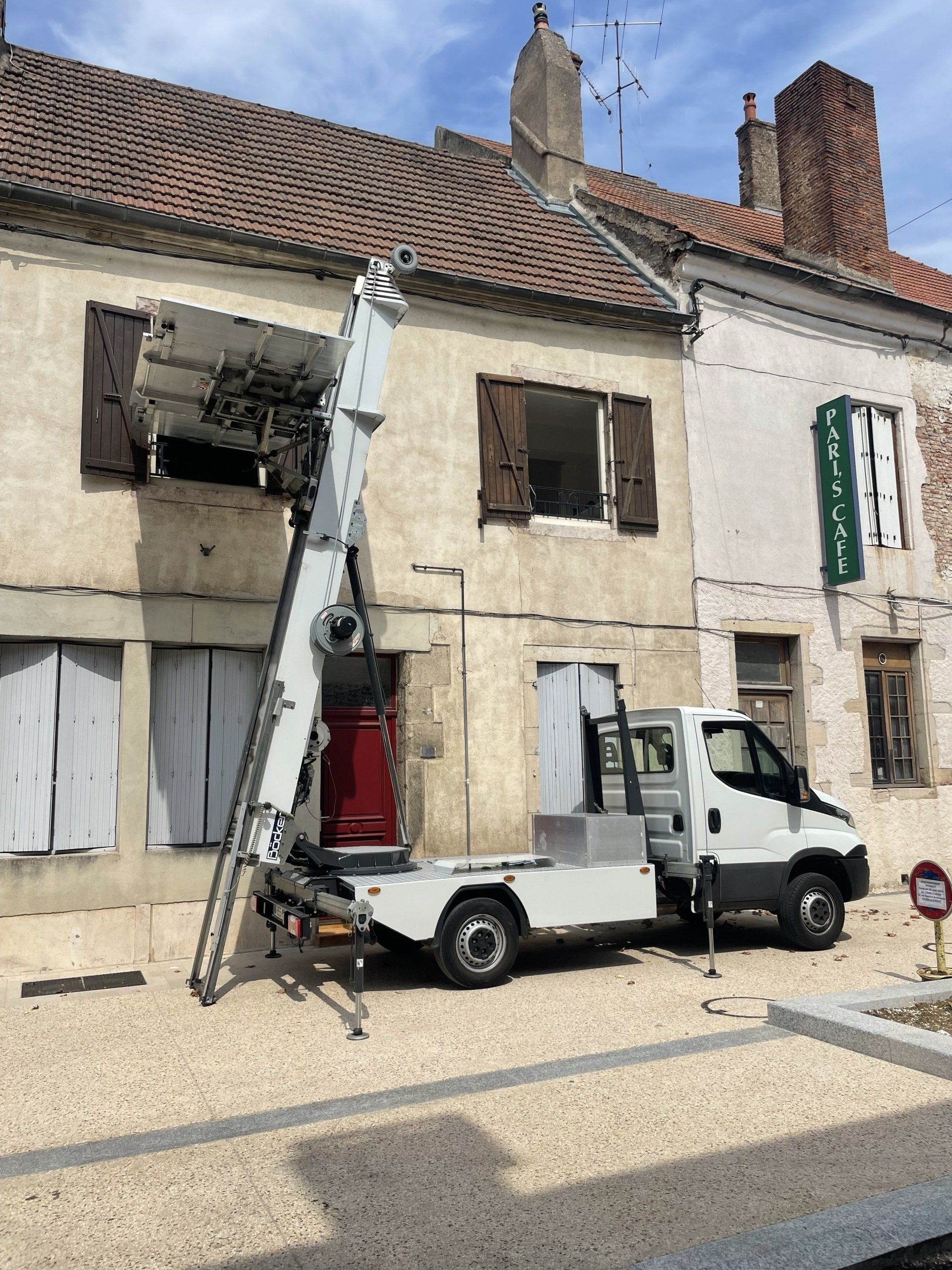 Un camion blanc avec une échelle attachée à l'arrière est garé devant un bâtiment.