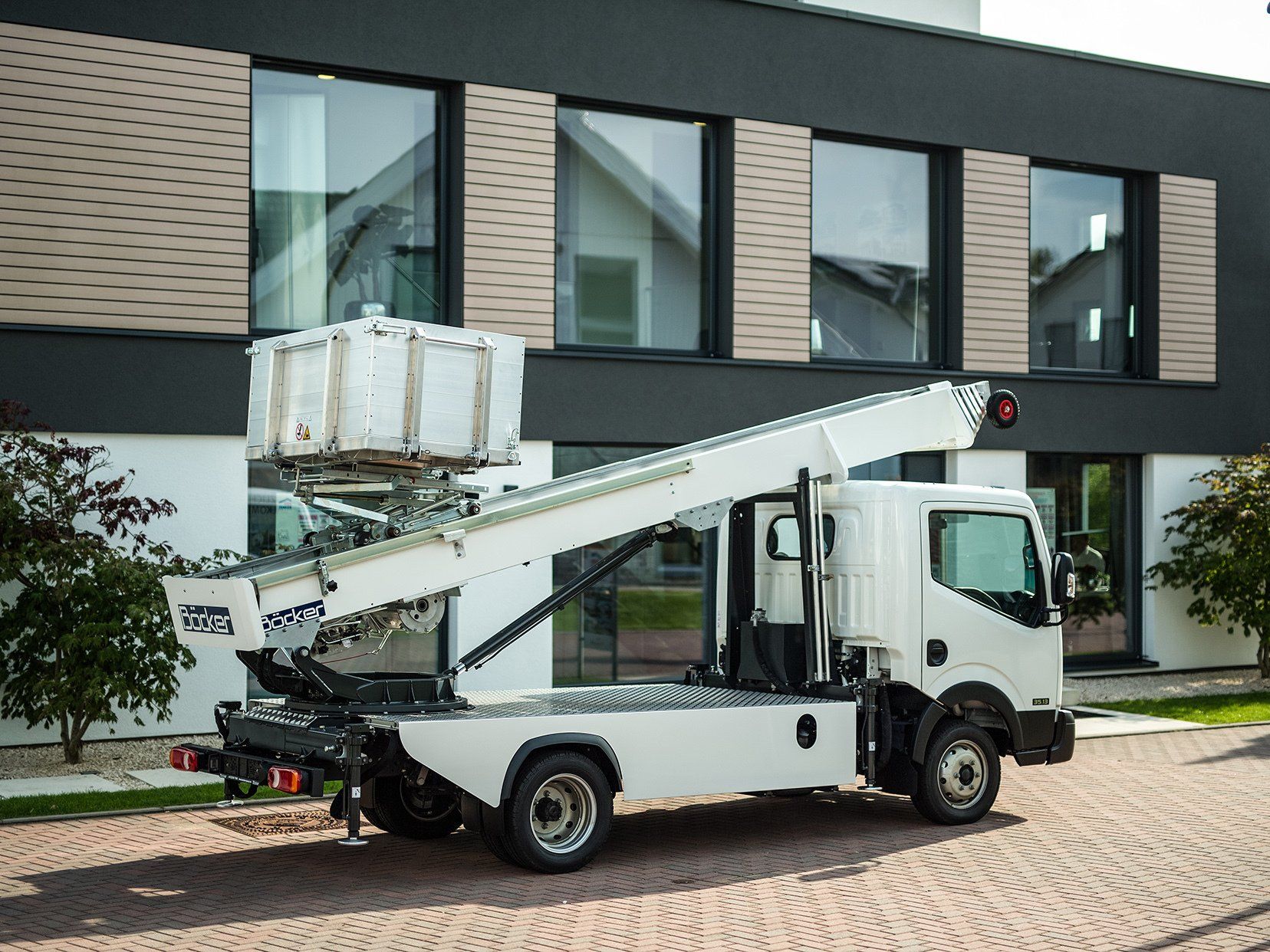 Un camion blanc avec une échelle à l'arrière est garé devant un bâtiment.