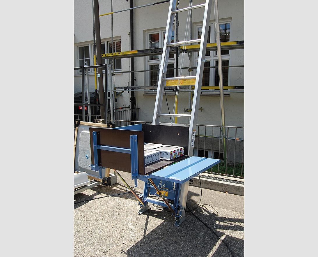 Un chariot bleu avec une échelle attachée est garé devant un bâtiment.