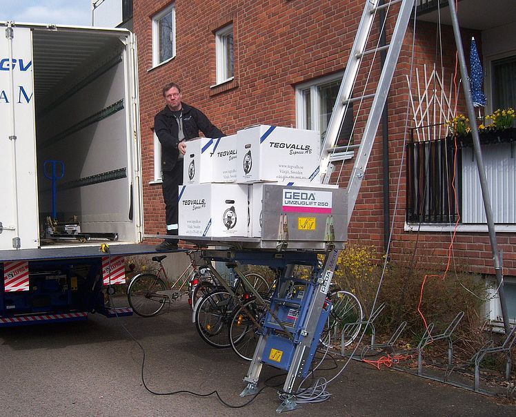 Un homme charge des cartons sur un ascenseur devant un camion de transport