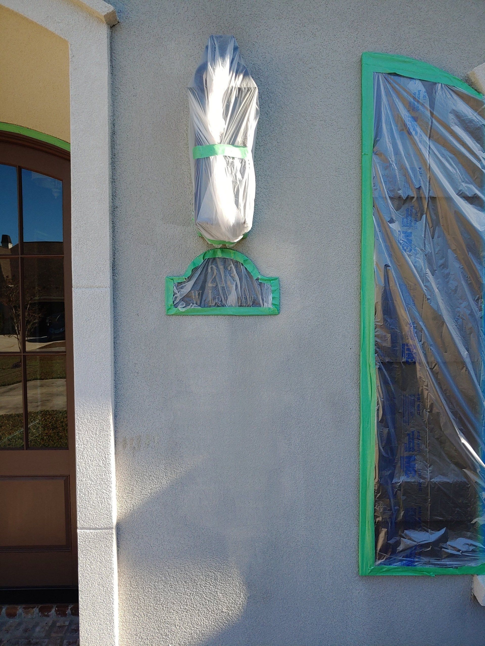 A statue is wrapped in plastic and hanging on the side of a building.