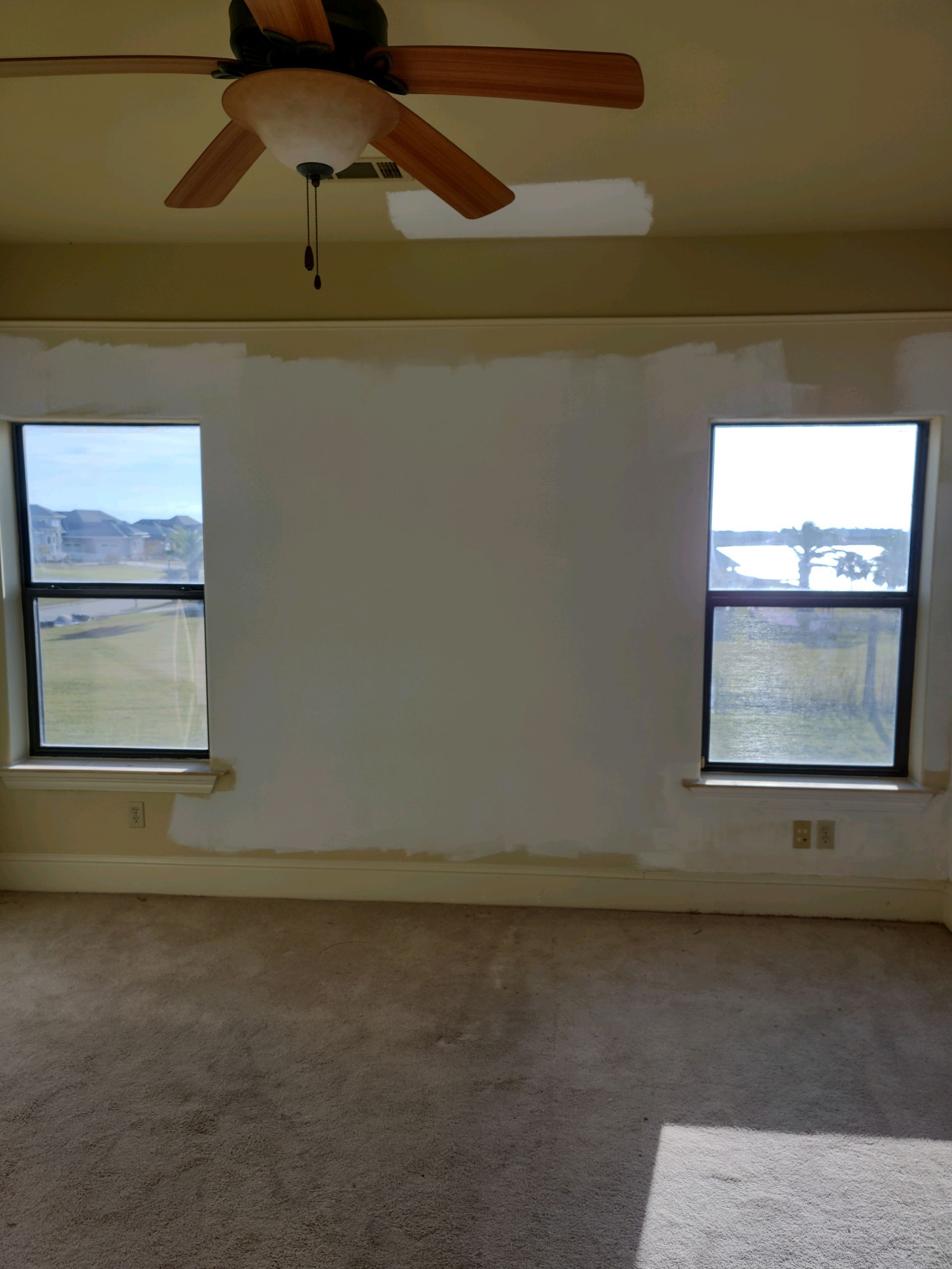 An empty room with two windows and a ceiling fan.
