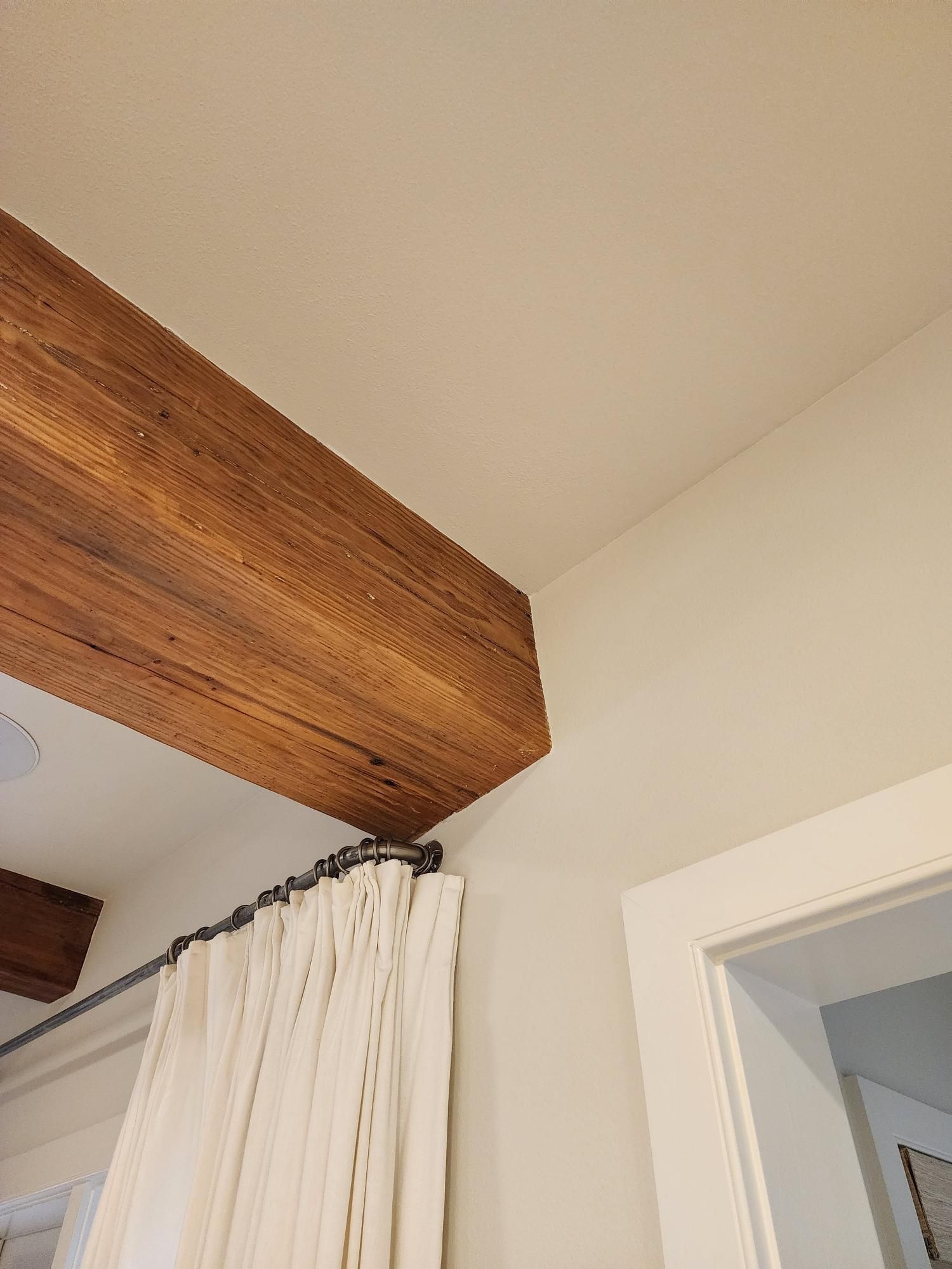 A wooden beam is hanging from the ceiling above a white curtain.