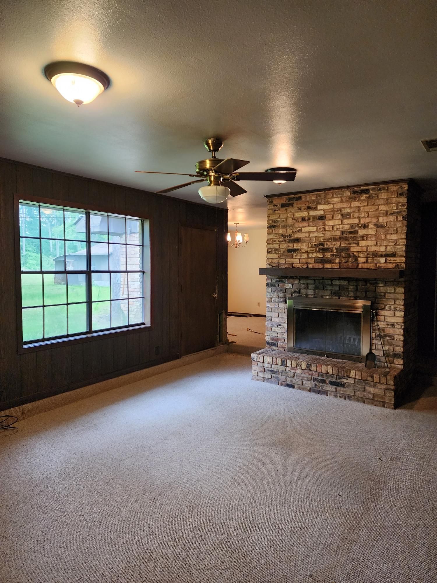 An empty living room with a fireplace and a ceiling fan.