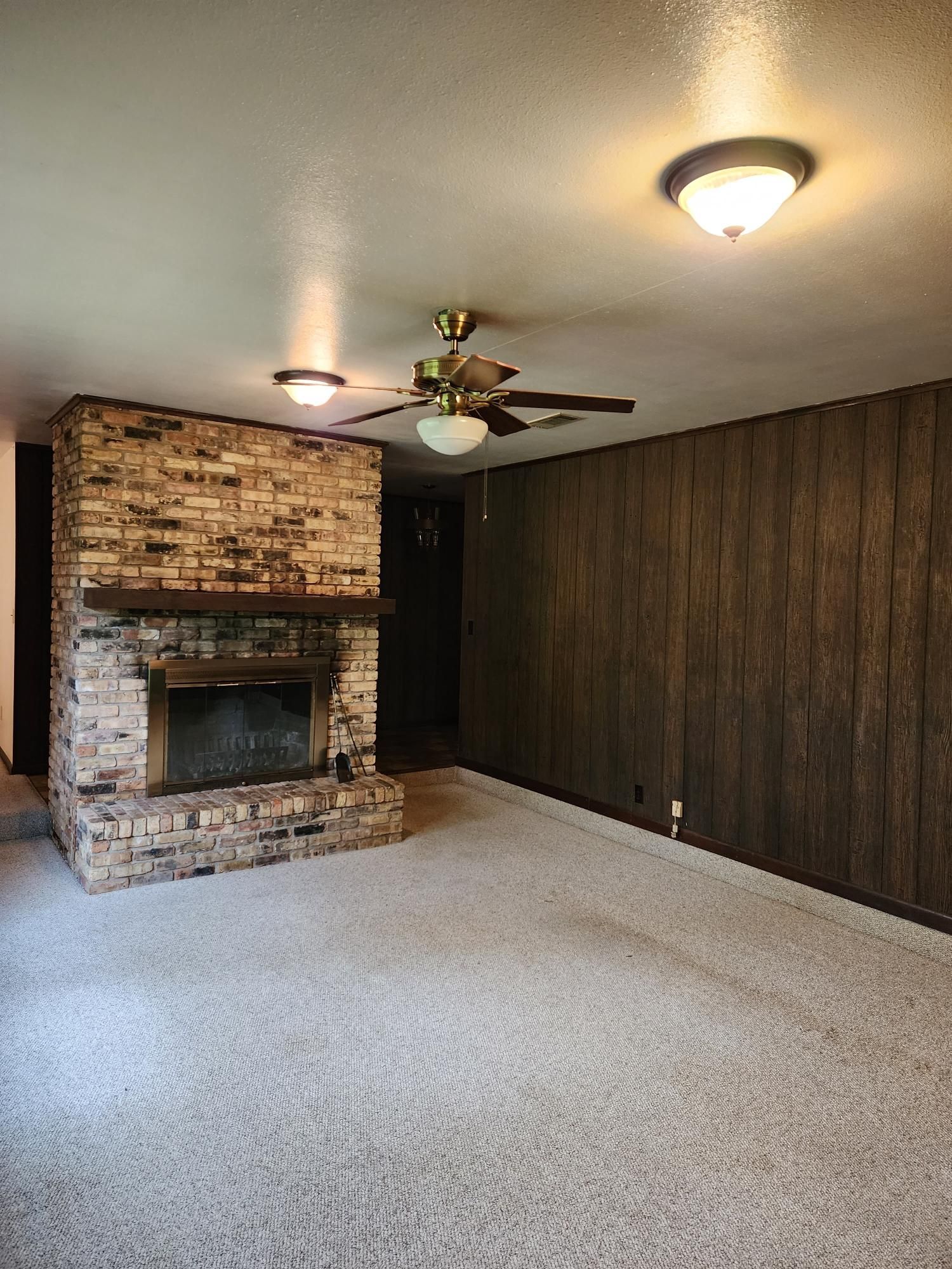 An empty living room with a fireplace and a ceiling fan.