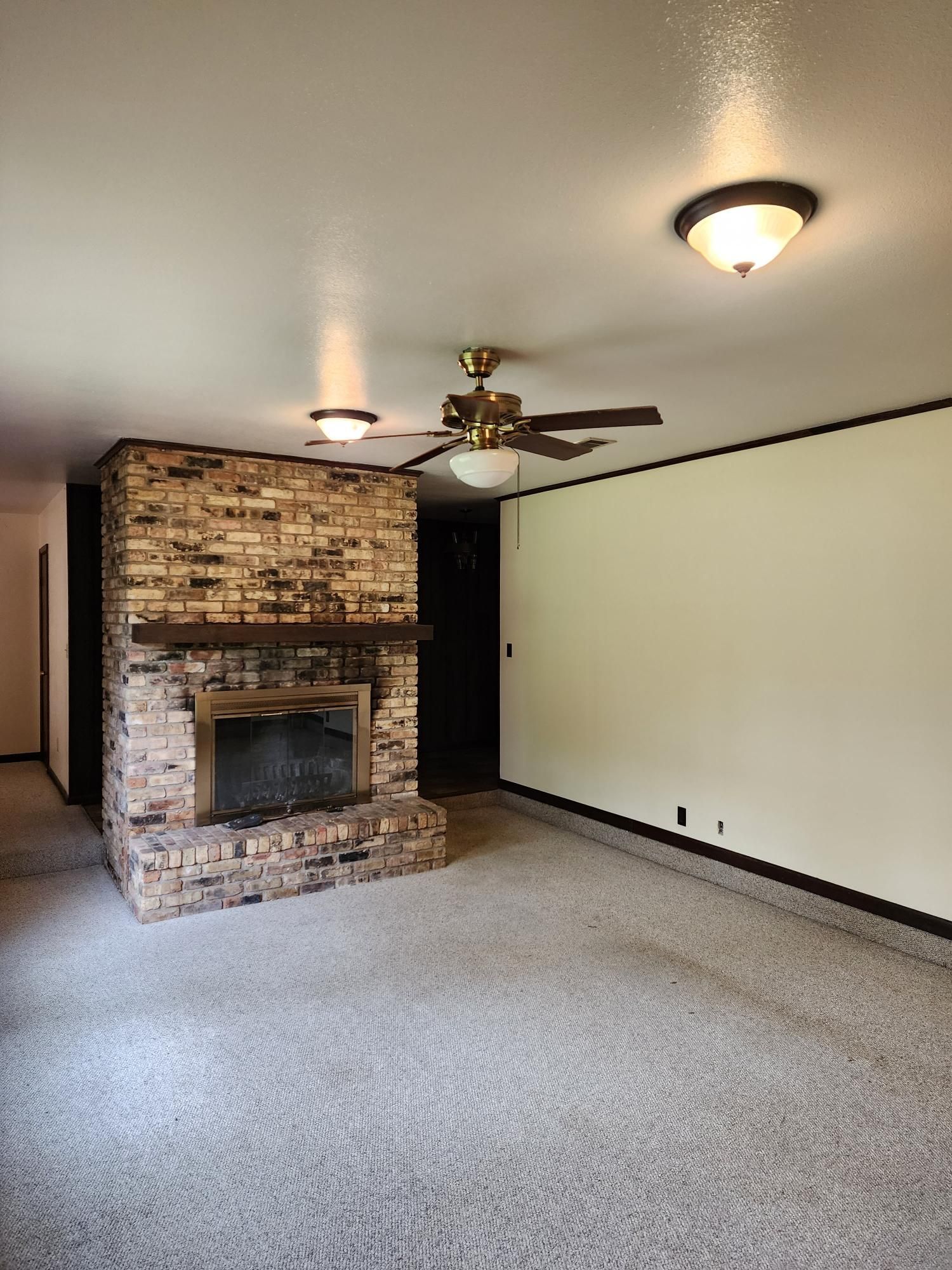 An empty living room with a fireplace and a ceiling fan.