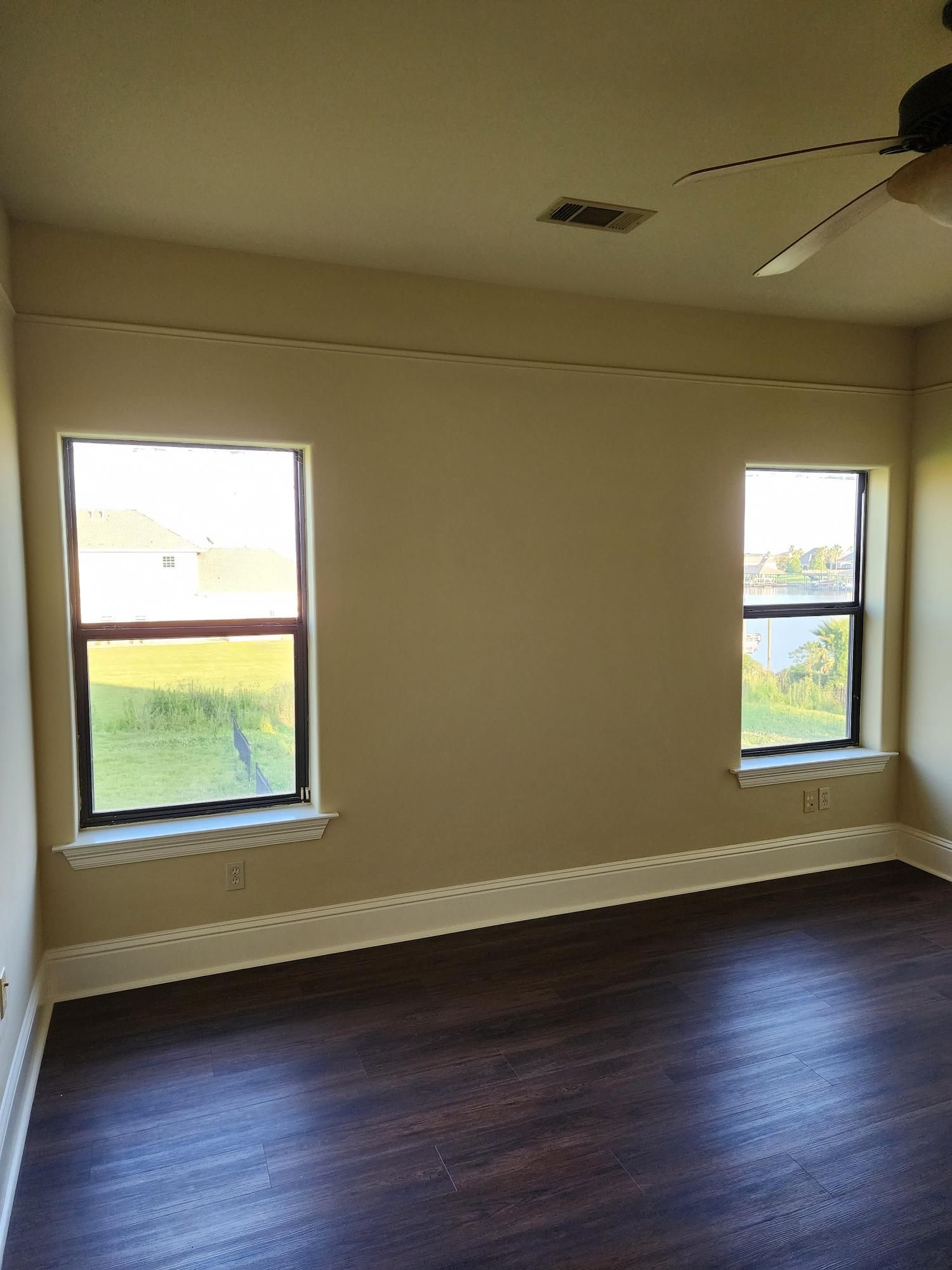 An empty room with two windows and a ceiling fan.