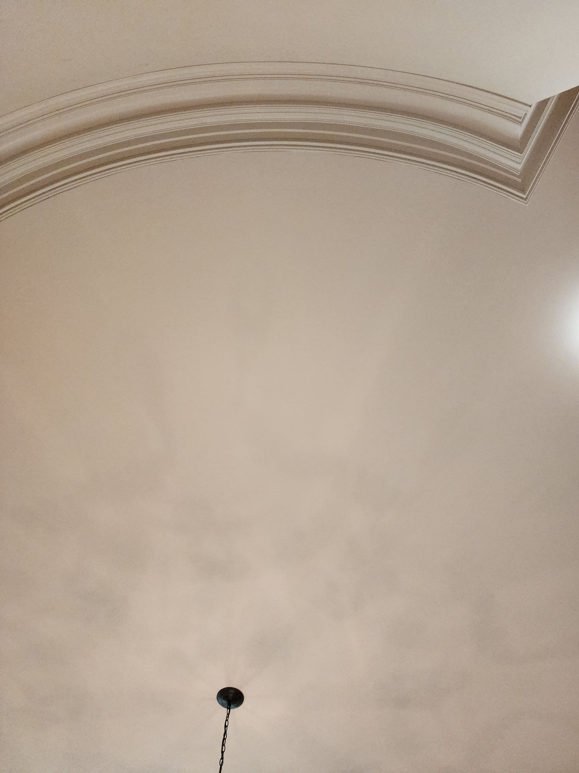 A white ceiling with a curved molding and a chandelier hanging from it.