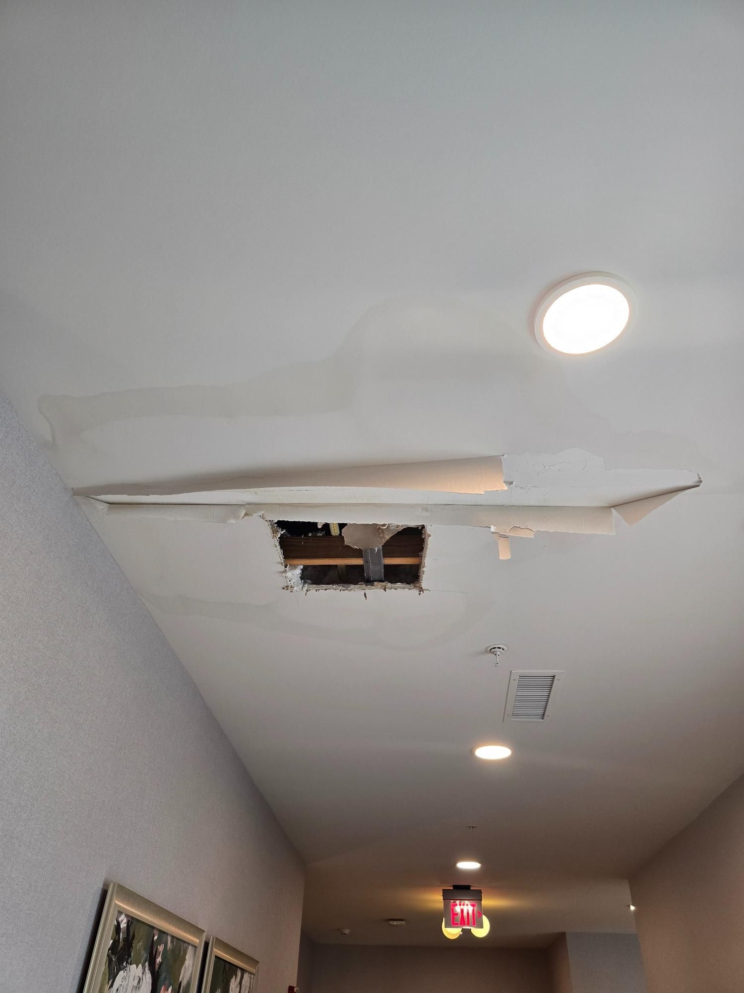 There is a hole in the ceiling in a hallway.