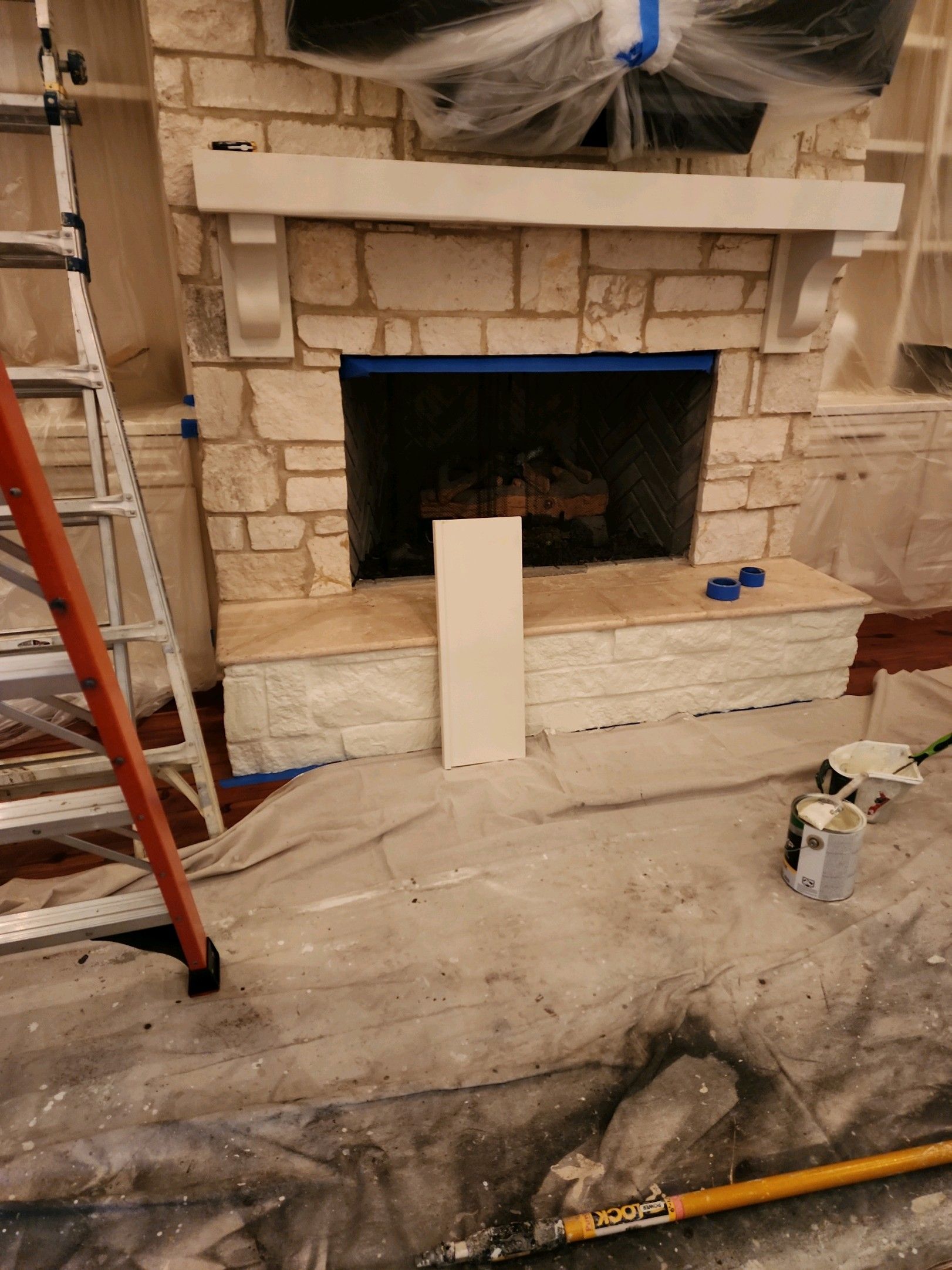 A fireplace is being painted in a living room with a ladder.