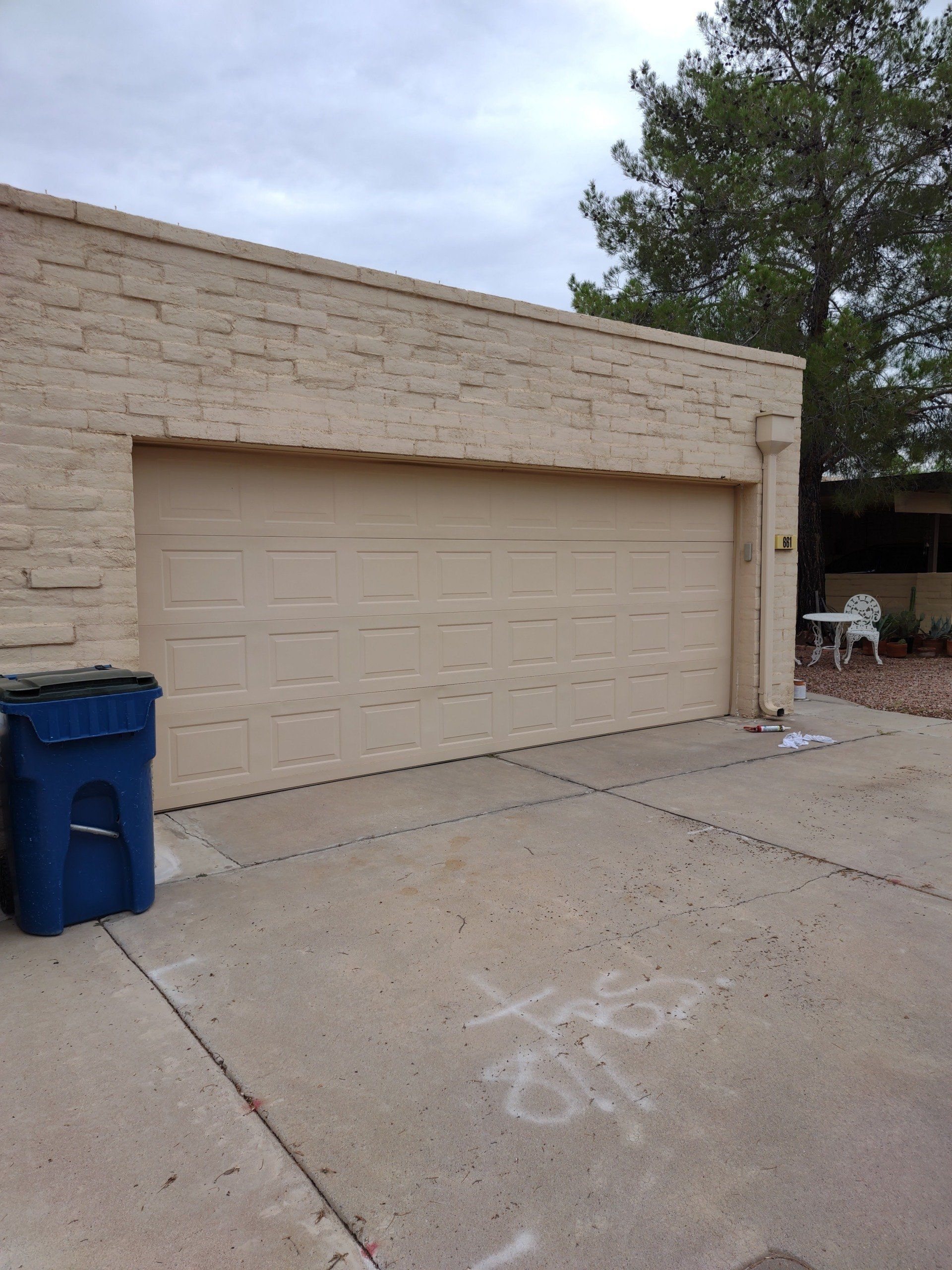 A blue trash can sits in front of a garage door