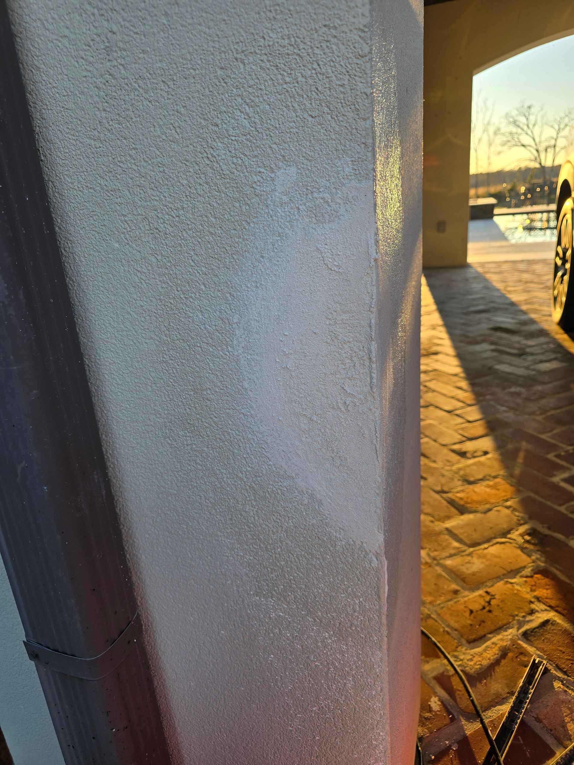 A close up of a white wall with a brick walkway in the background