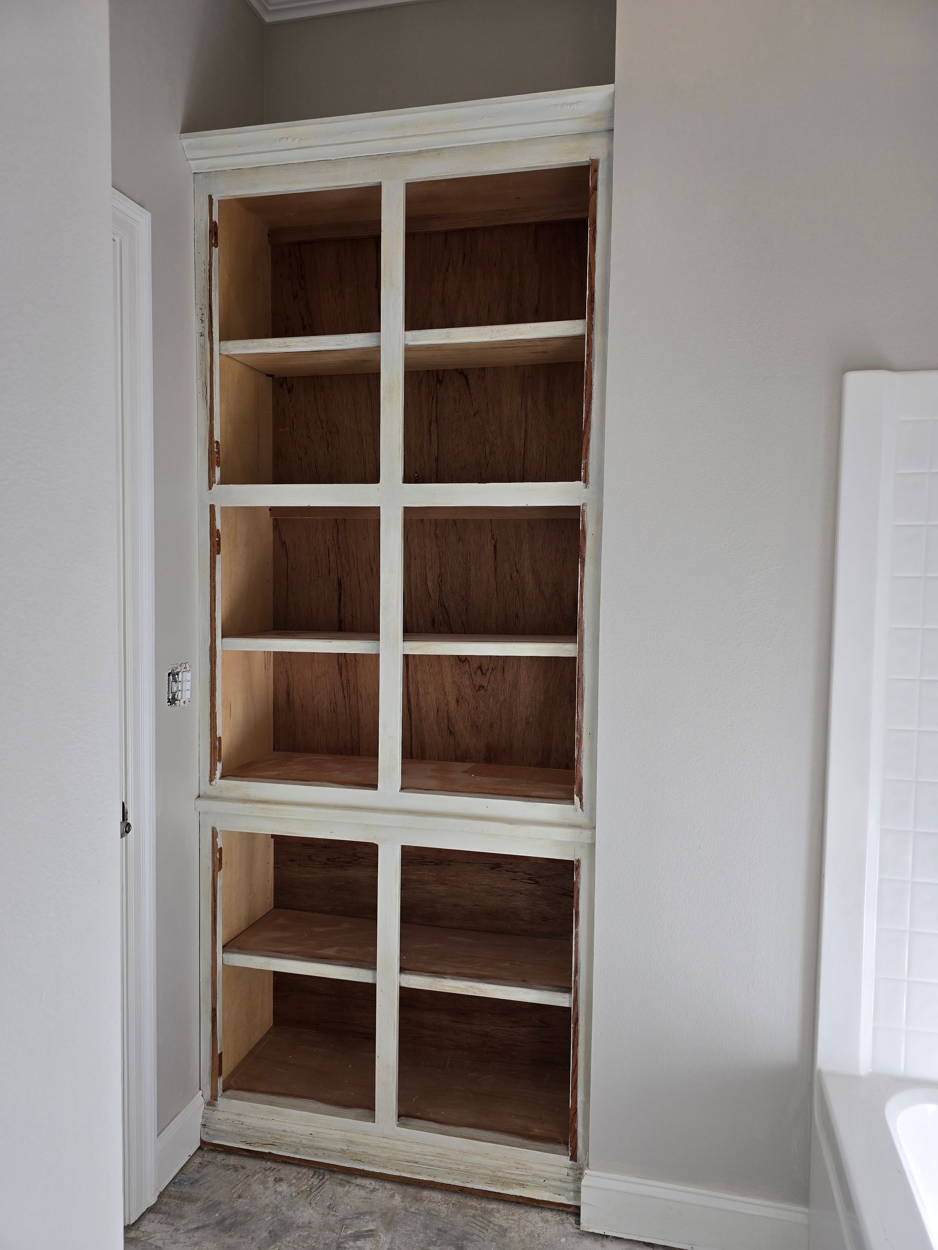 A closet with a lot of shelves and a bathtub in the background