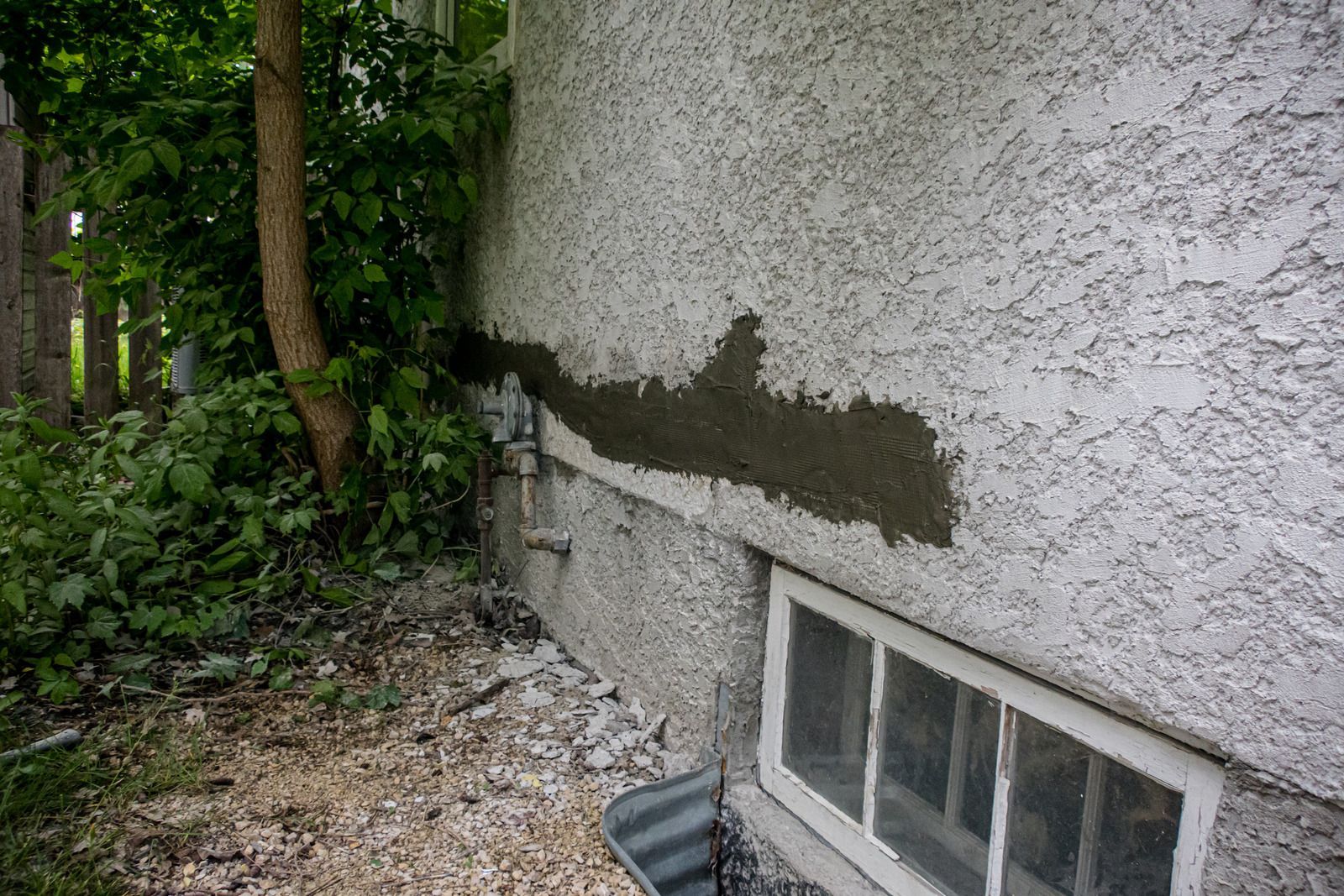 A concrete wall with a window and a tree in the background.