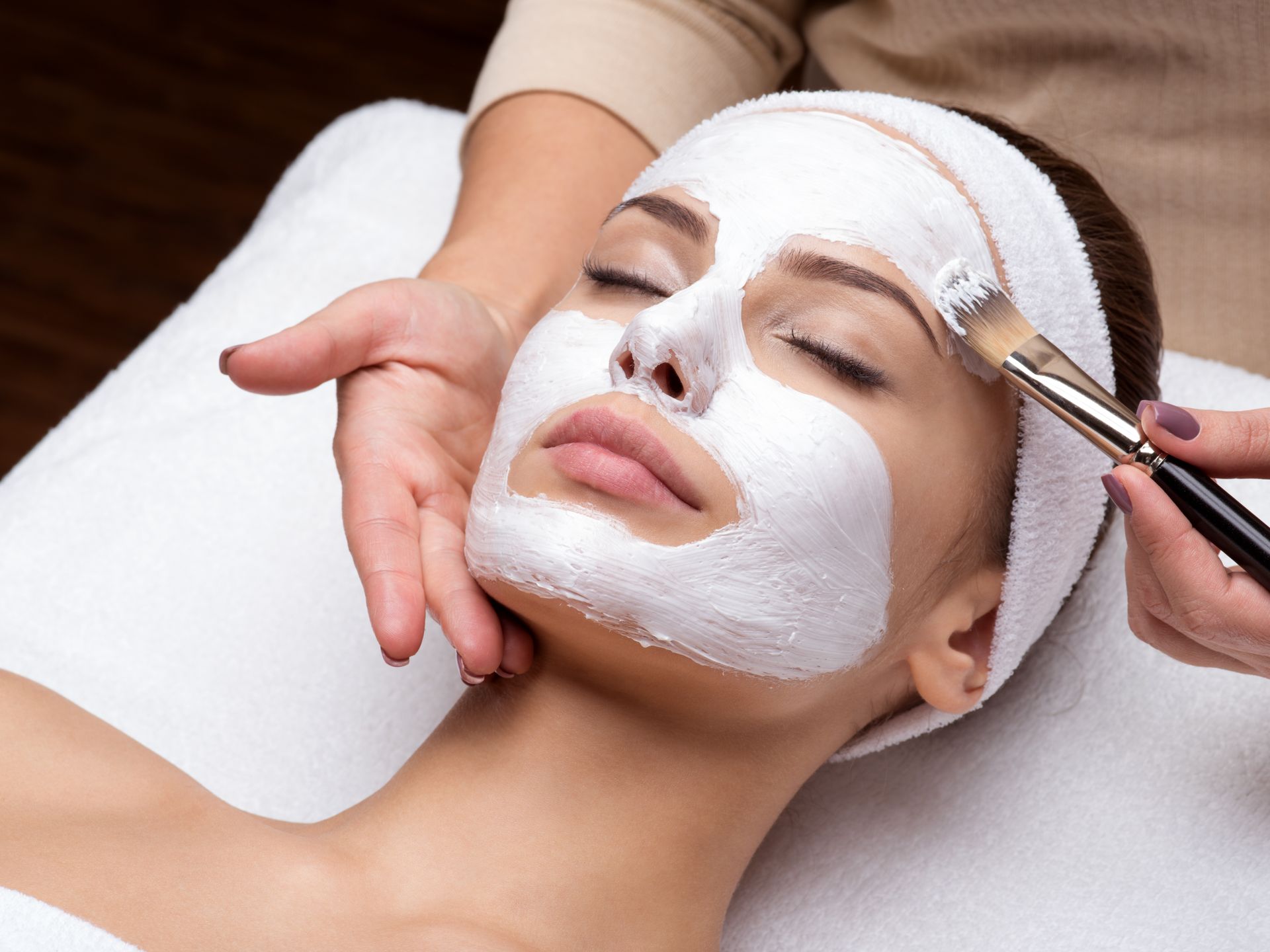 Facial mask treatment being applied with a brush while the client lies on a spa bed