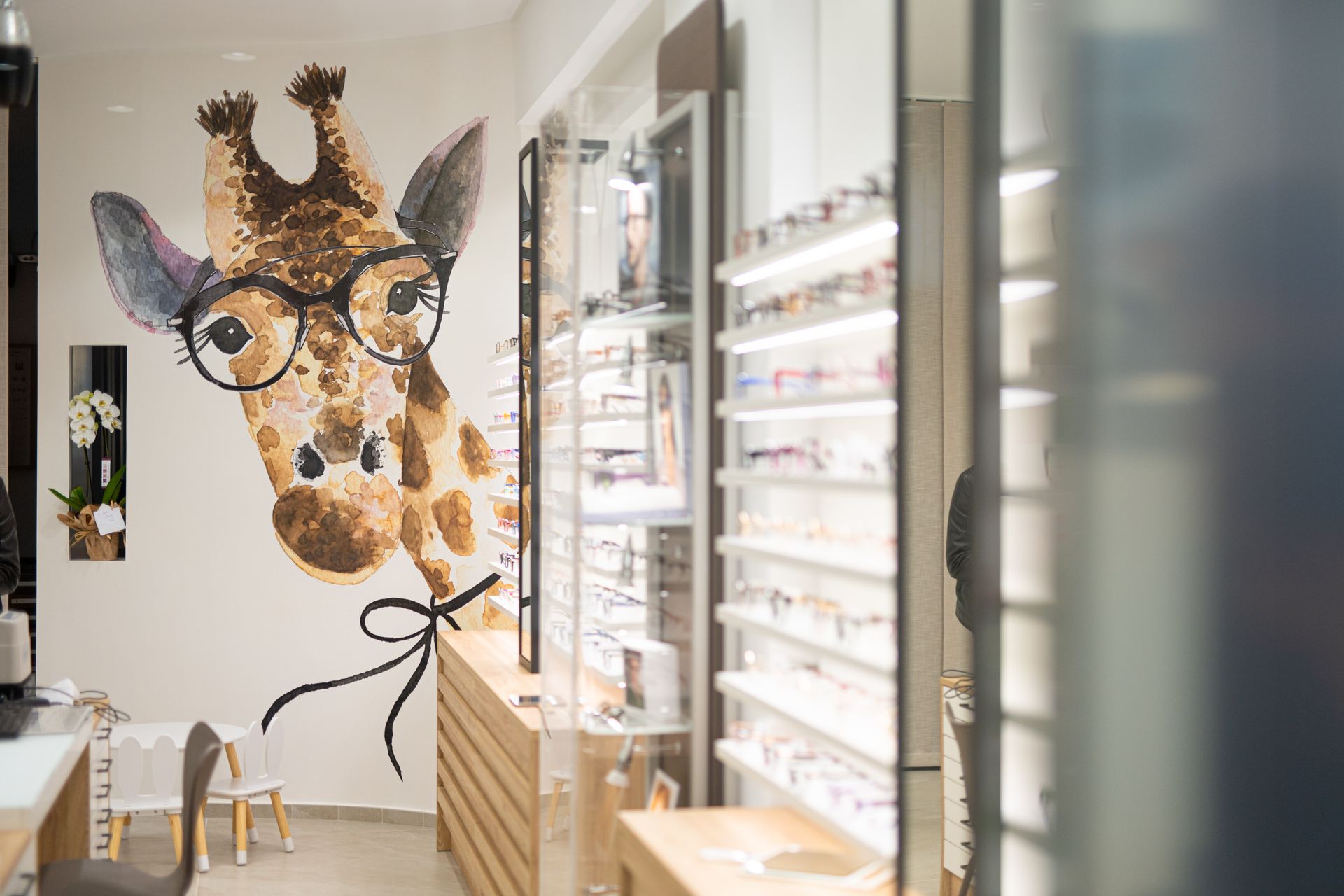 Murale raffigurante una giraffa che indossa occhiali in un negozio di occhiali con scaffali pieni di montature.