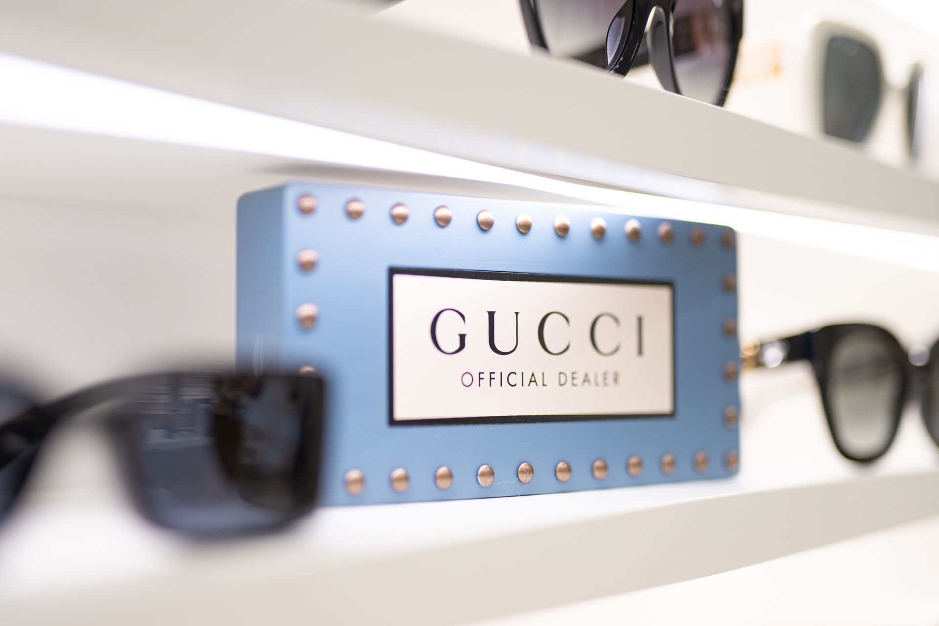 Cartello blu del rivenditore ufficiale Gucci sullo scaffale con occhiali da sole.