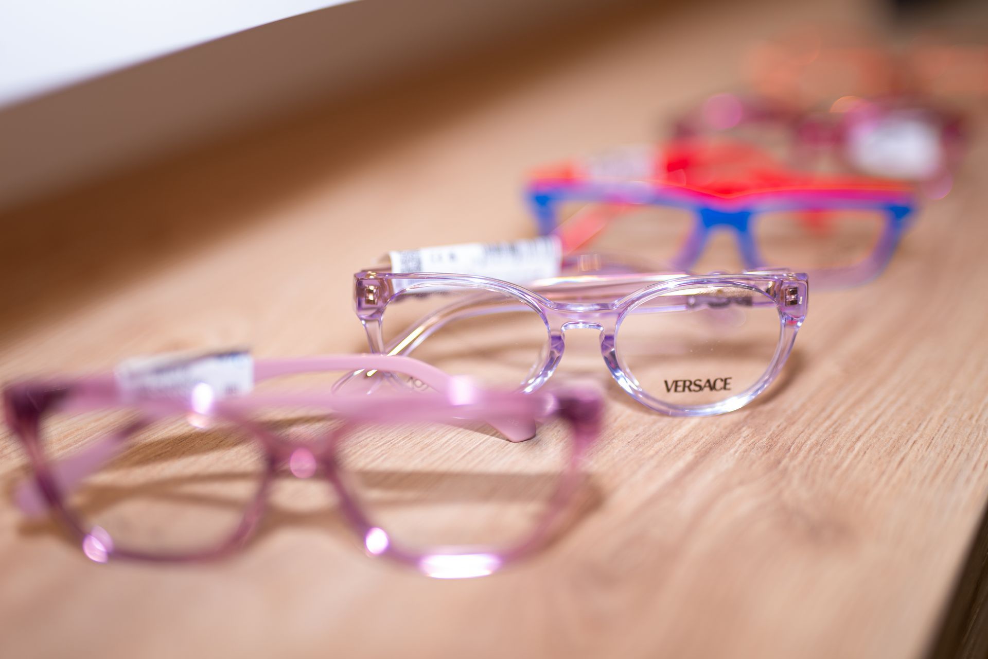 Quattro montature di occhiali colorati su una superficie di legno. Rosa, lavanda, blu e rosso.