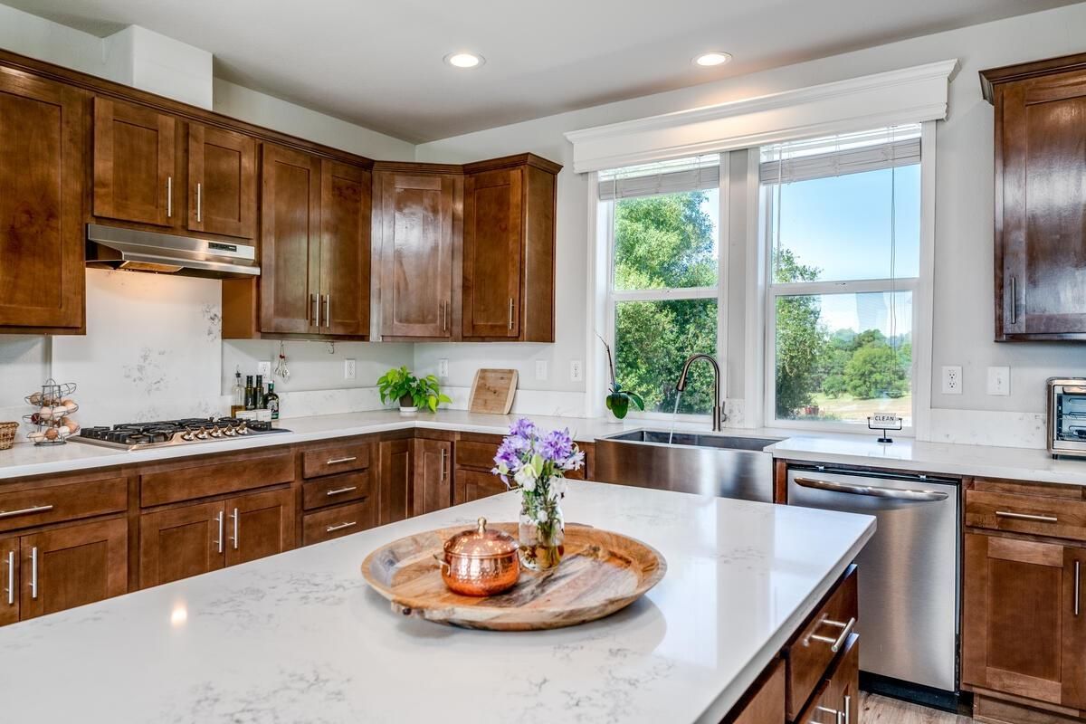A kitchen with wooden cabinets , white counter tops , stainless steel appliances and a large island.