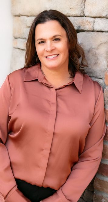 A woman in a pink shirt is standing in front of a brick wall.